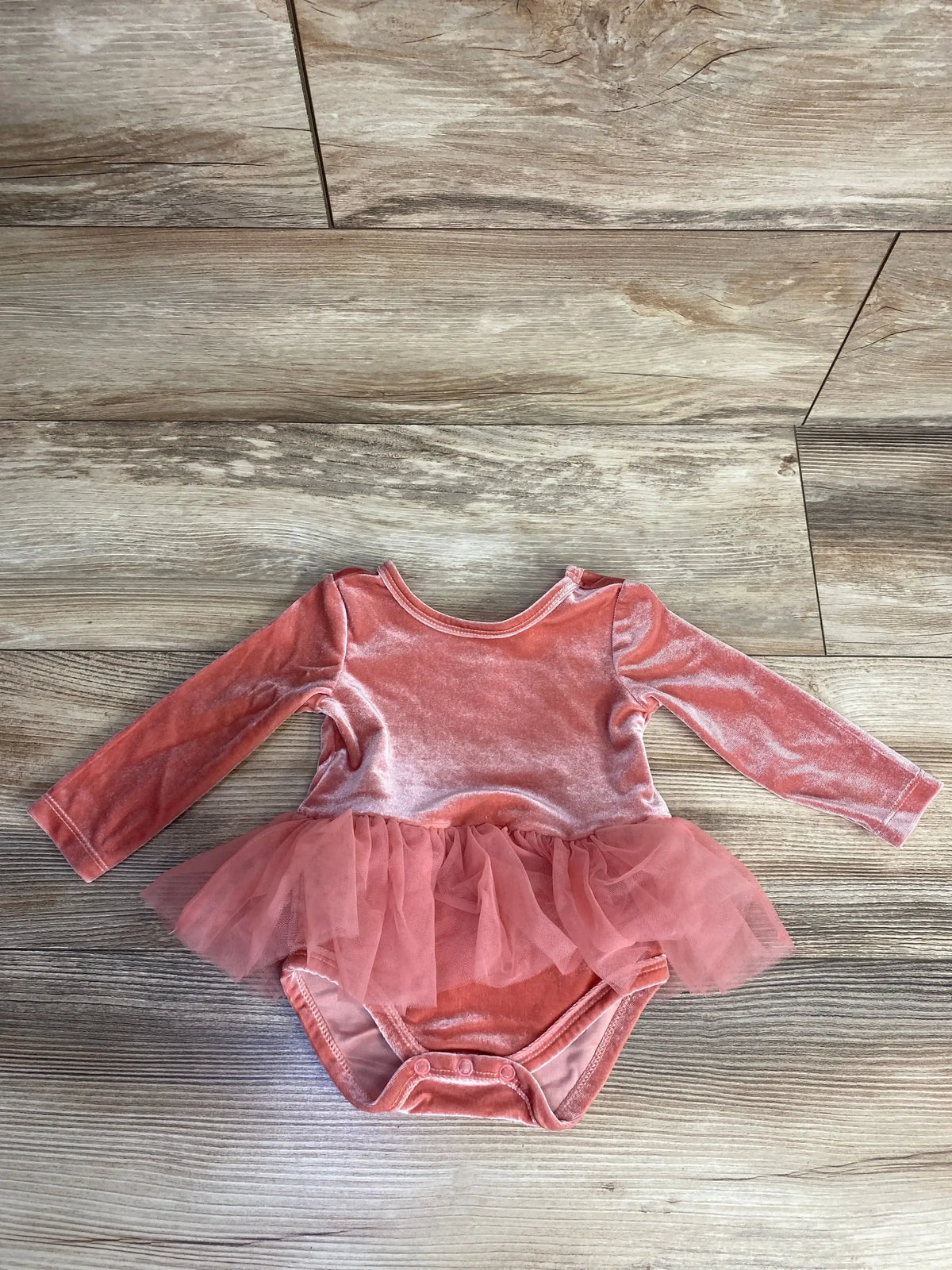 Pink velvet baby bodysuit with long sleeves and tutu skirt on wooden floor