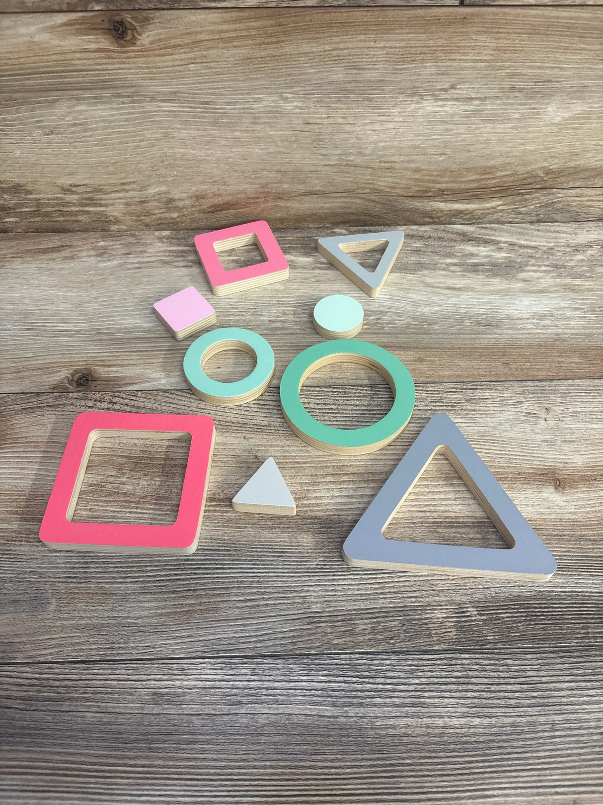 Overhead view of KiwiCo Panda Crate shape puzzle pieces showing painted wooden rings, squares, and triangles on a wood background