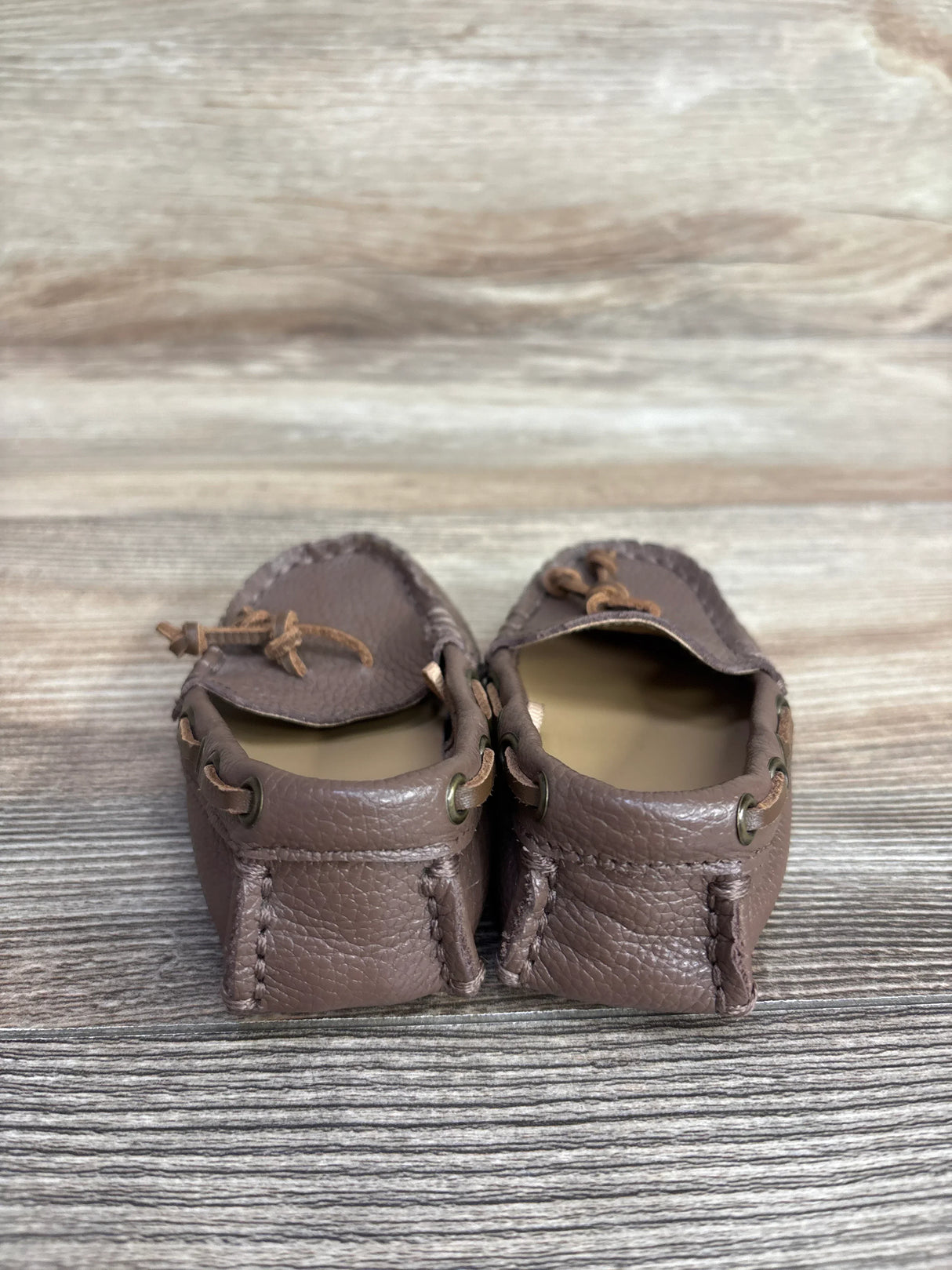 Pair of brown leather moccasin loafers on wooden surface with decorative laces