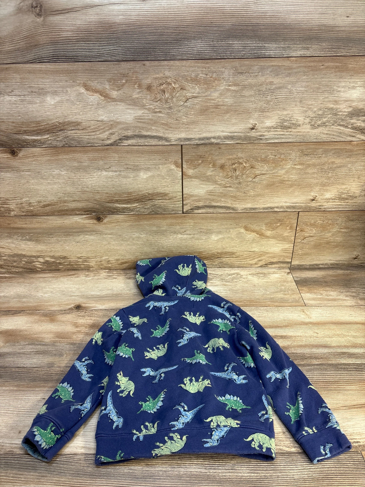 Blue kids hoodie with green and blue dinosaur print, laid on wood floor