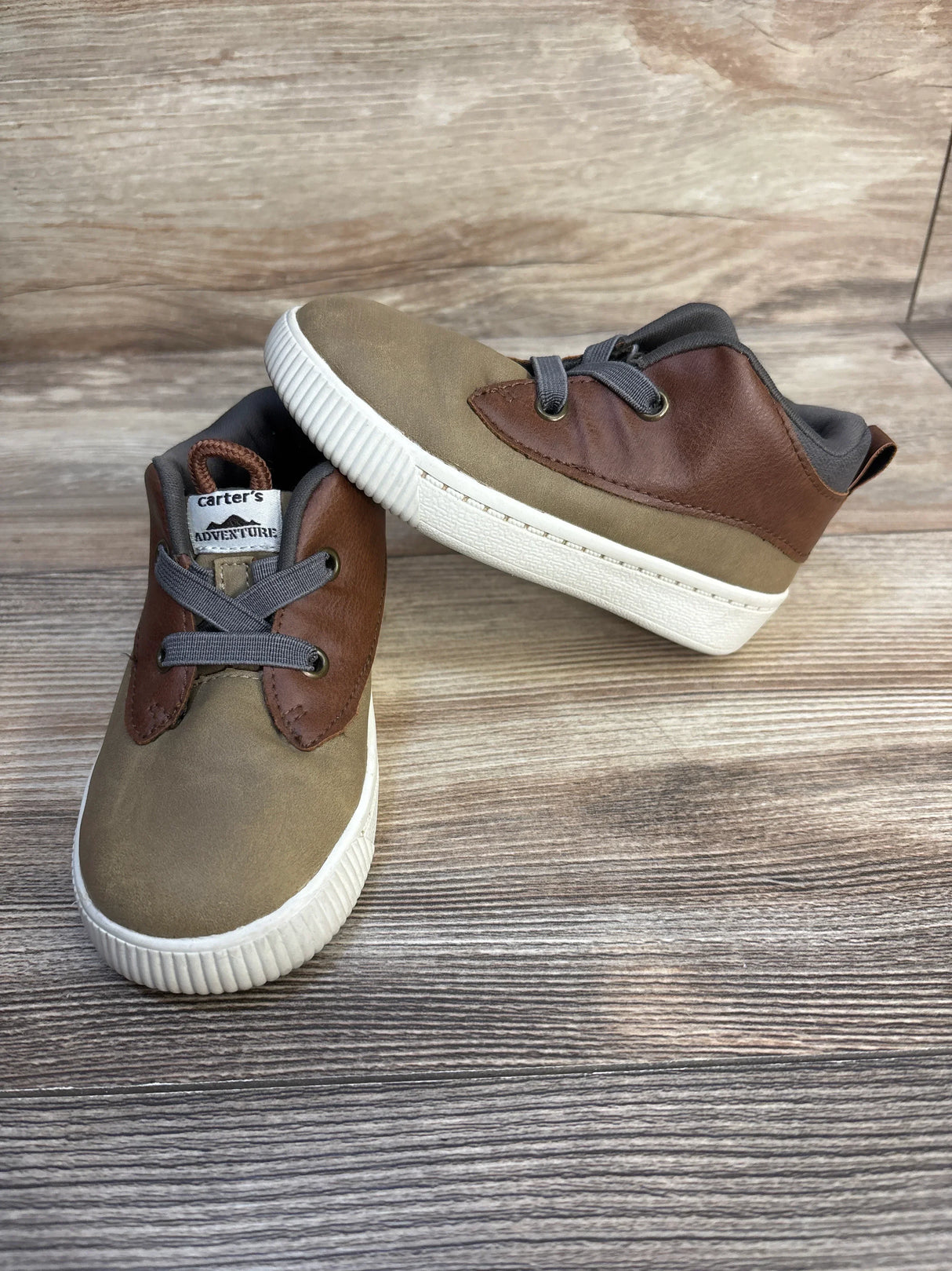 Brown and tan Carter's toddler shoes with gray laces on wood background