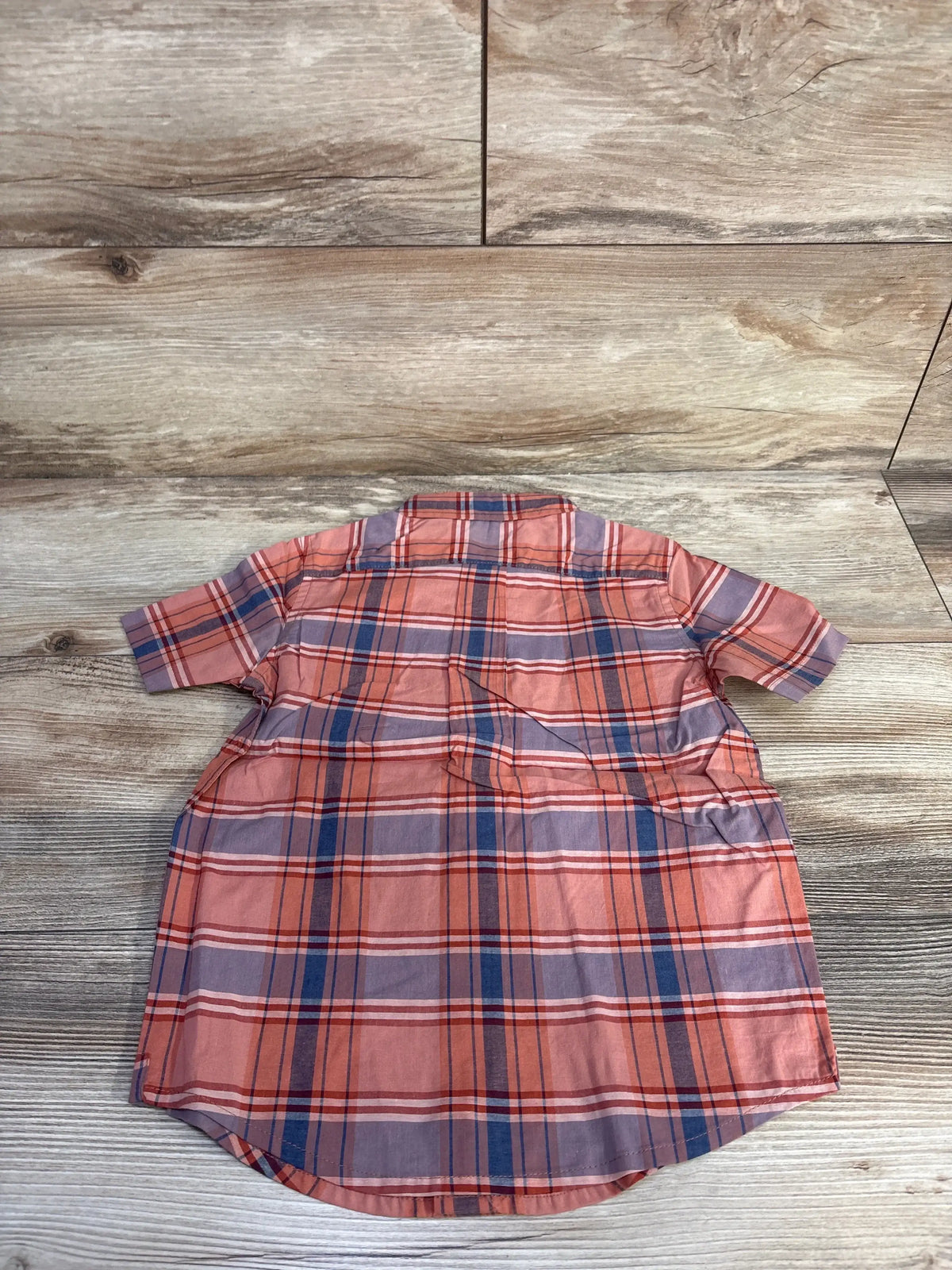 Back view of toddler plaid button-down shirt in orange and blue with short sleeves and curved hem on light wood background