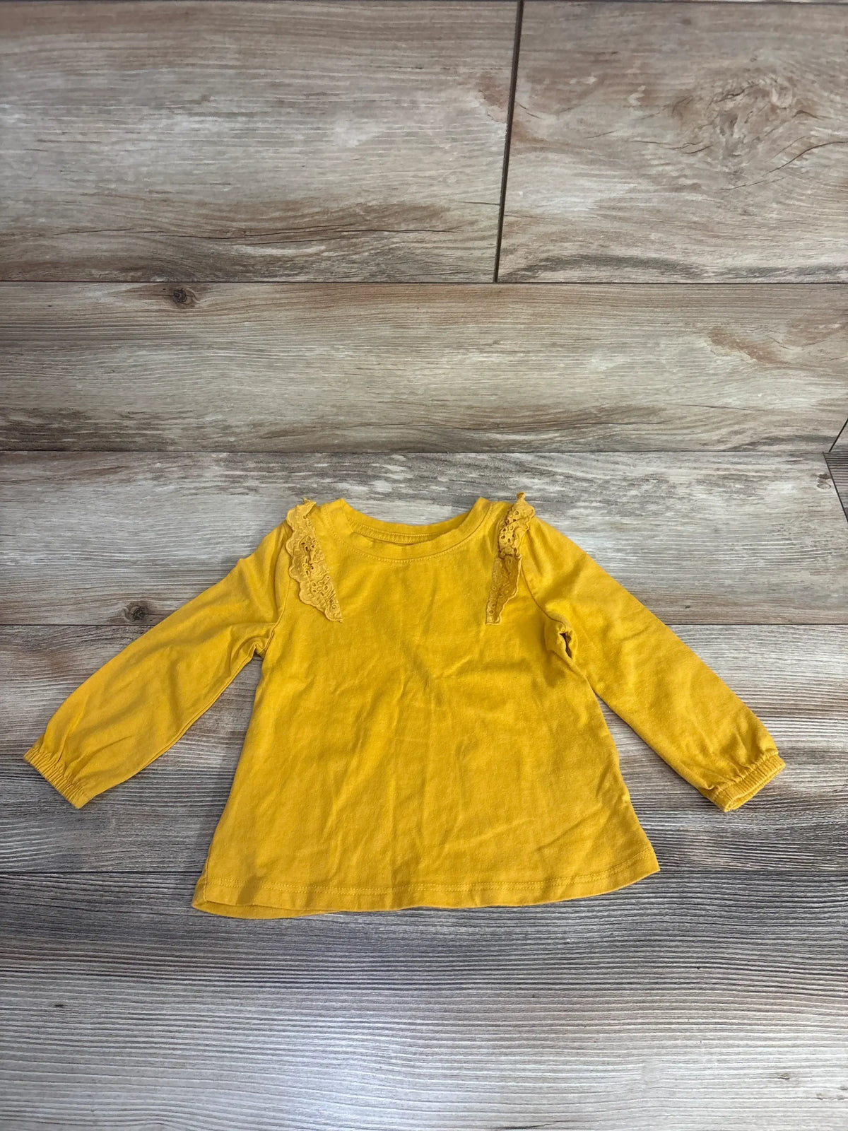 Yellow long-sleeve toddler shirt with lace trim on wooden floor