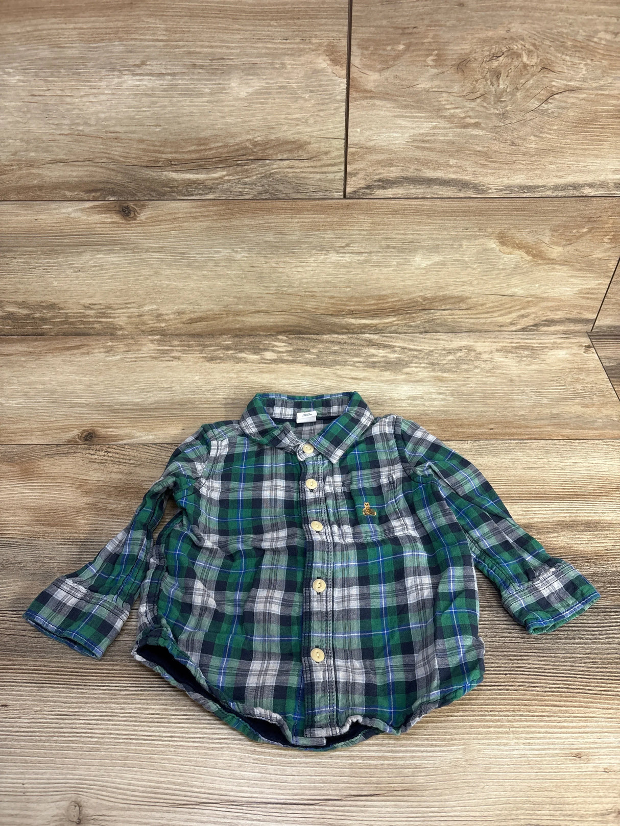 Green plaid baby button-down shirt with long sleeves on wood floor