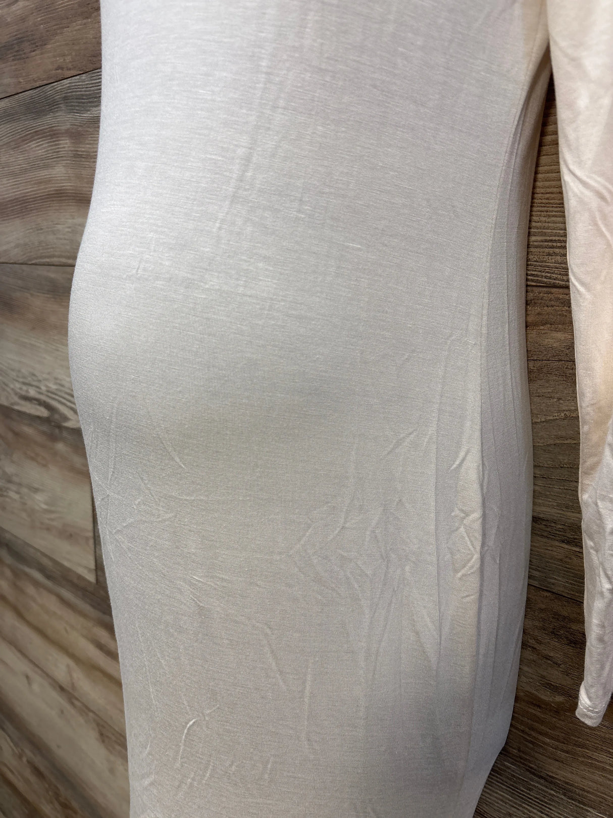 Close-up of white fitted dress on mannequin with visible fabric texture, wood background
