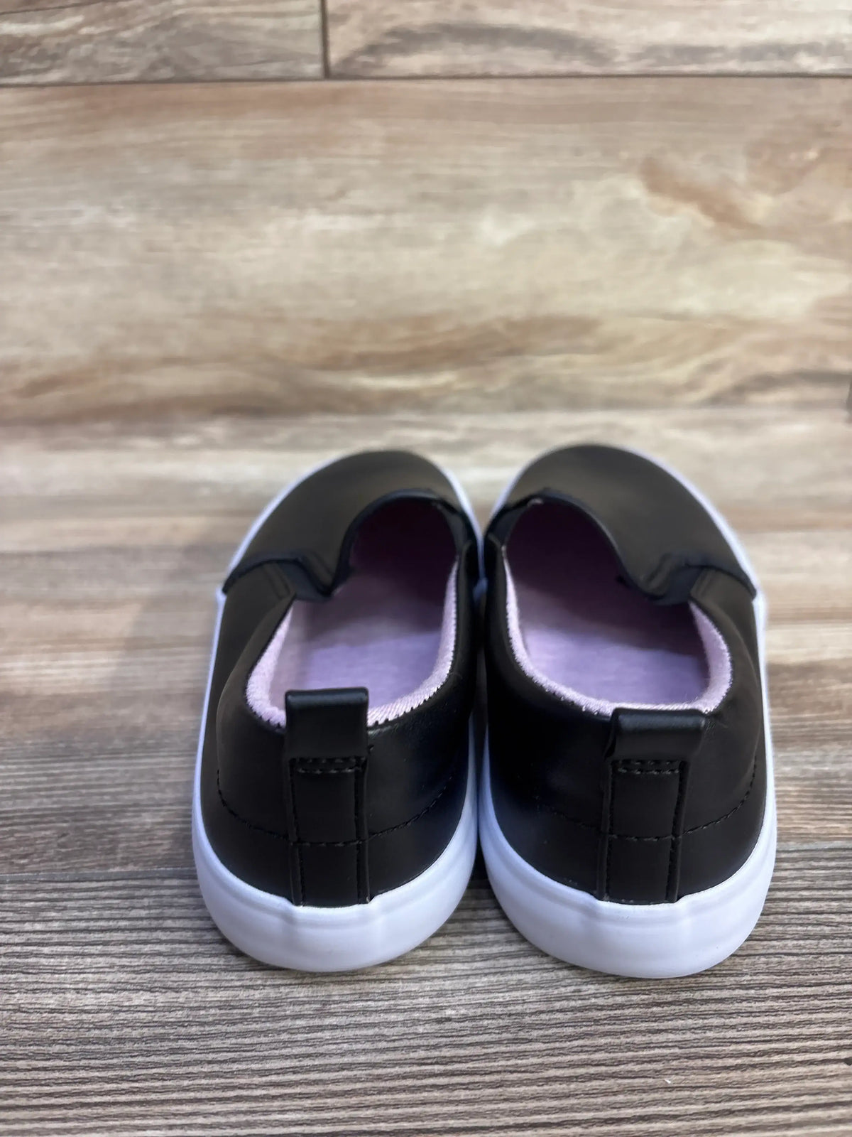 Rear view of Cat & Jack Hailey slip-on sneakers in black showing white soles and pink lining on wood floor size 4Y