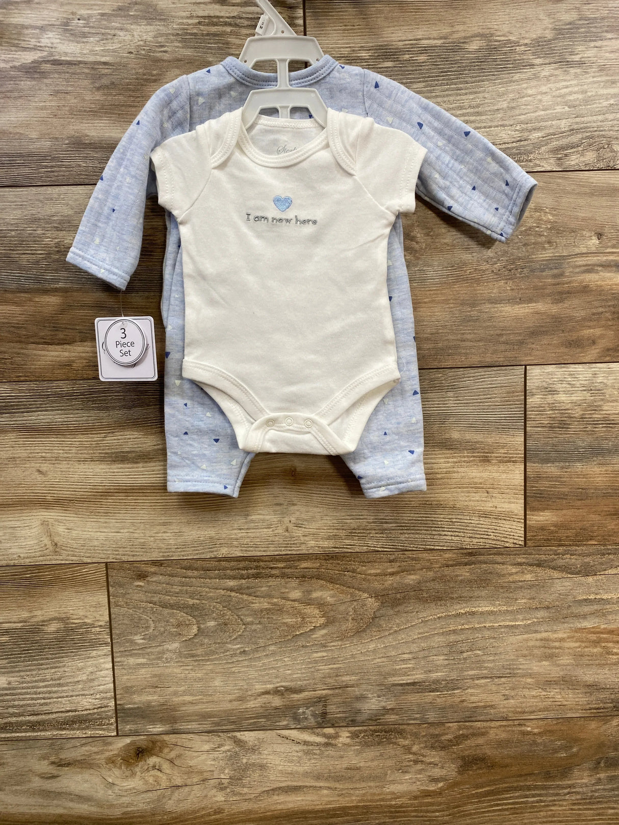 Baby onesie and sleeper set with blue heart and 'I am new here' text on wood background