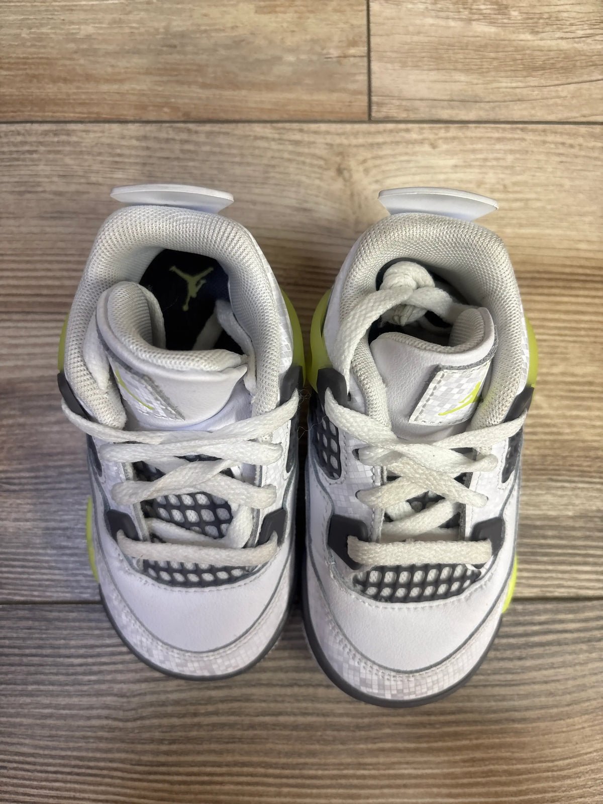 Top view of Air Jordan 4 Retro TD Light Lemon Twist sneakers, size 7C, with black accents on wood flooring