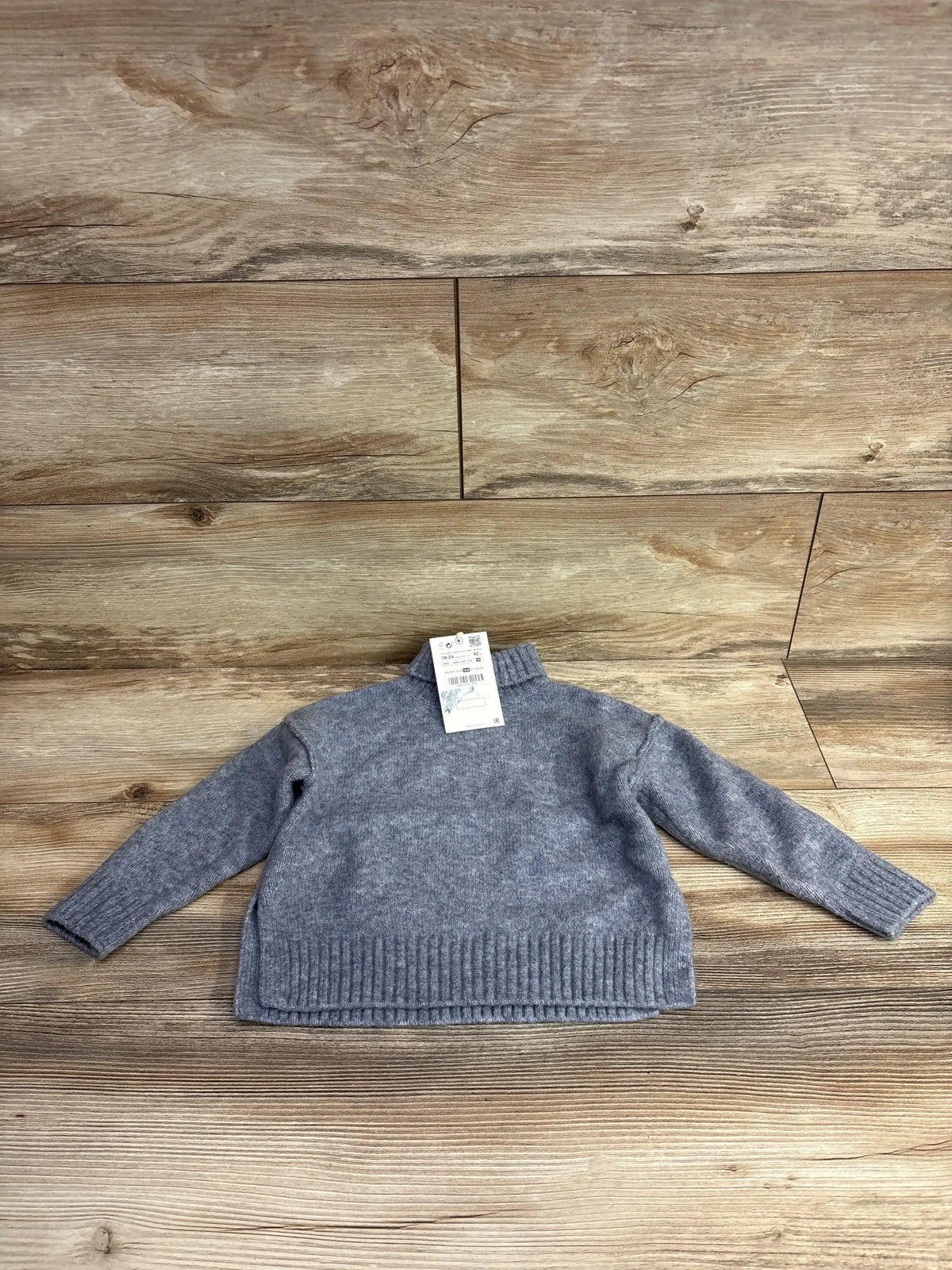 Flat lay of grey Zara toddler turtleneck sweater 18-24 months showing ribbed hem, cuffs, and mock neck on wood background