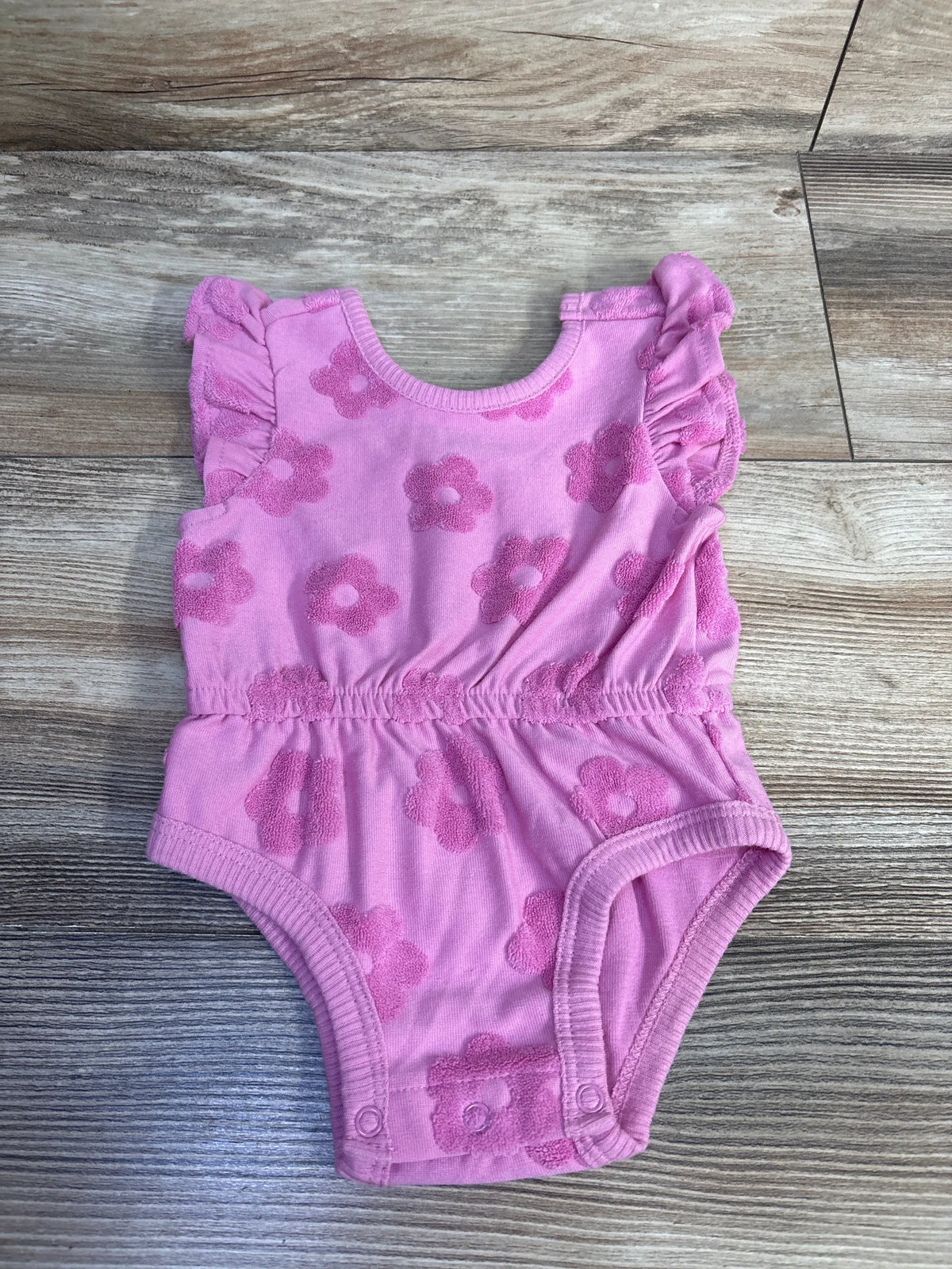 Front view of PL Baby pink bubble romper showcasing flower pattern and bubble hem on wood-grain background
