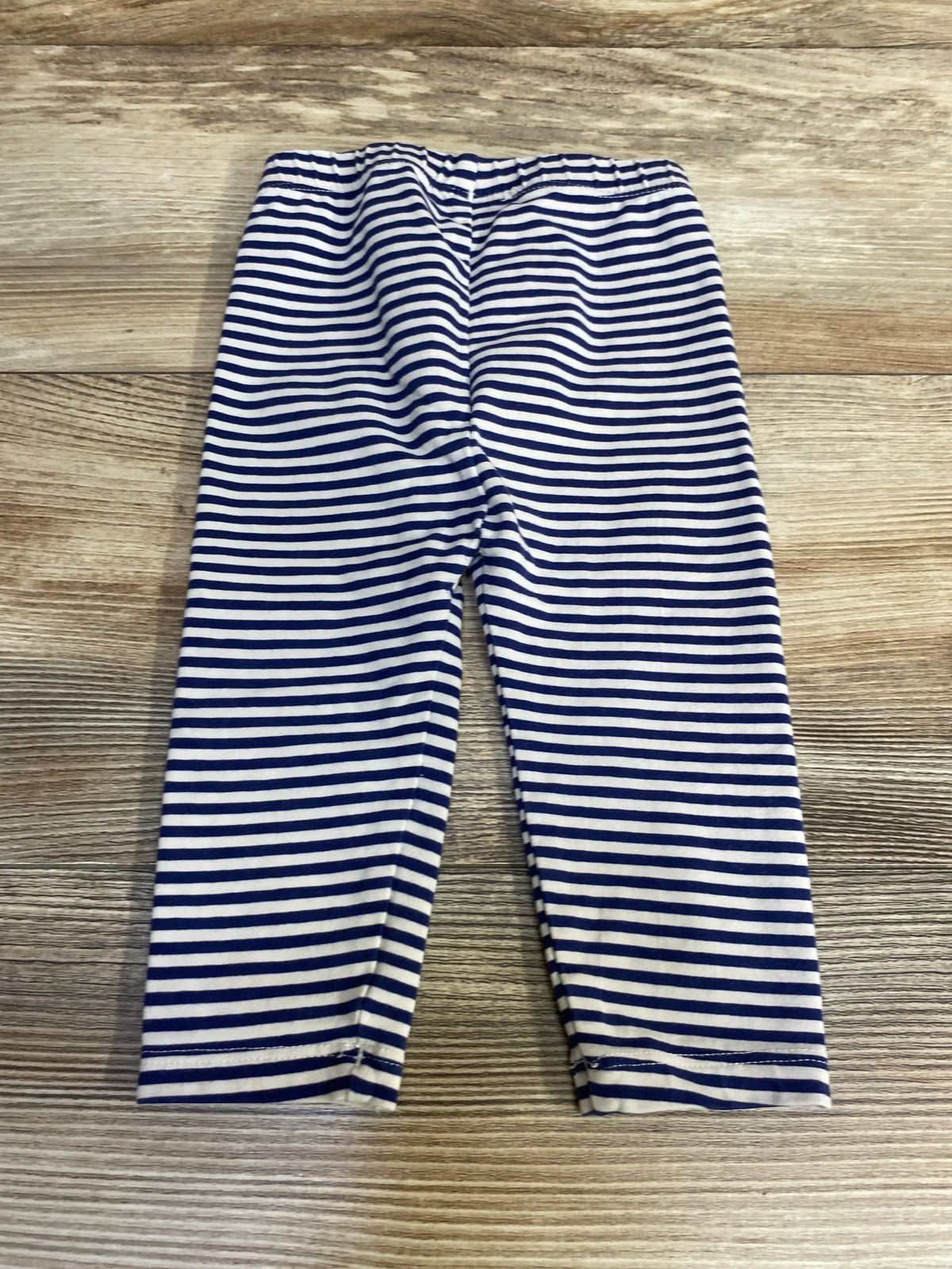Flat lay of Hanna Andersson navy striped leggings 3-6m showcasing white horizontal stripes on wood plank floor
