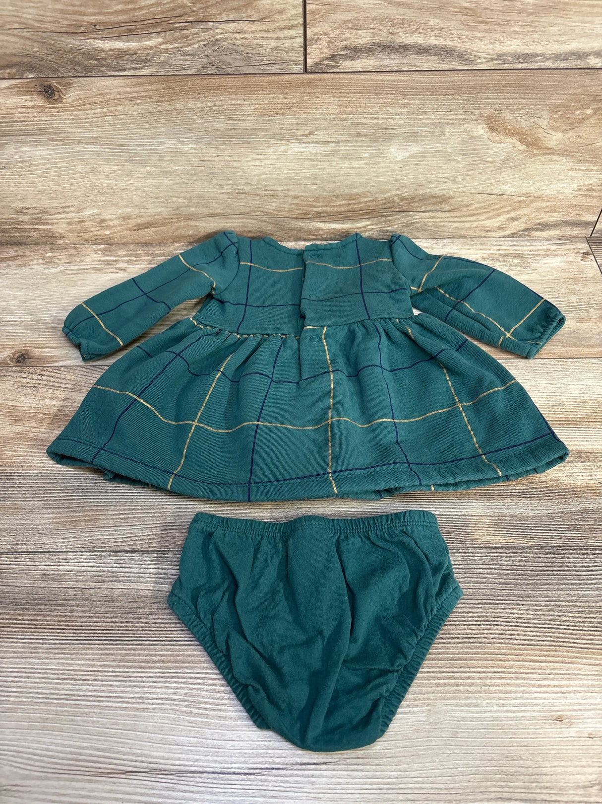 Flat lay of green fleece-lined long-sleeve baby dress and matching bloomers showing gold windowpane check on wood background