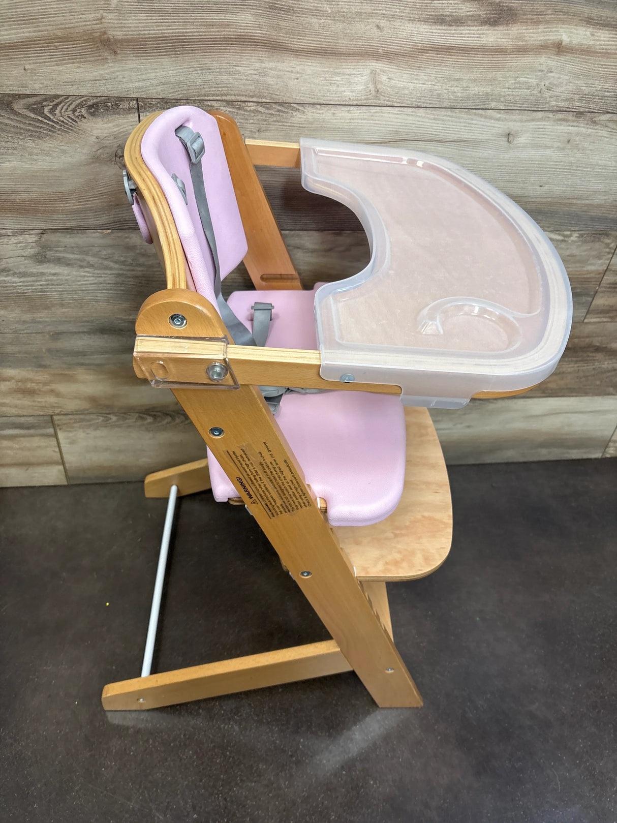 Wooden high chair with pink cushioning, safety straps, and clear plastic tray for babies