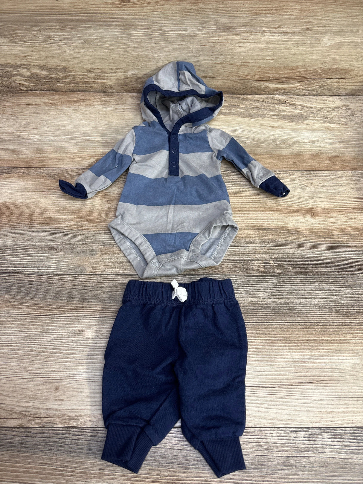 Striped blue and gray hooded baby onesie with navy blue pants on wooden floor