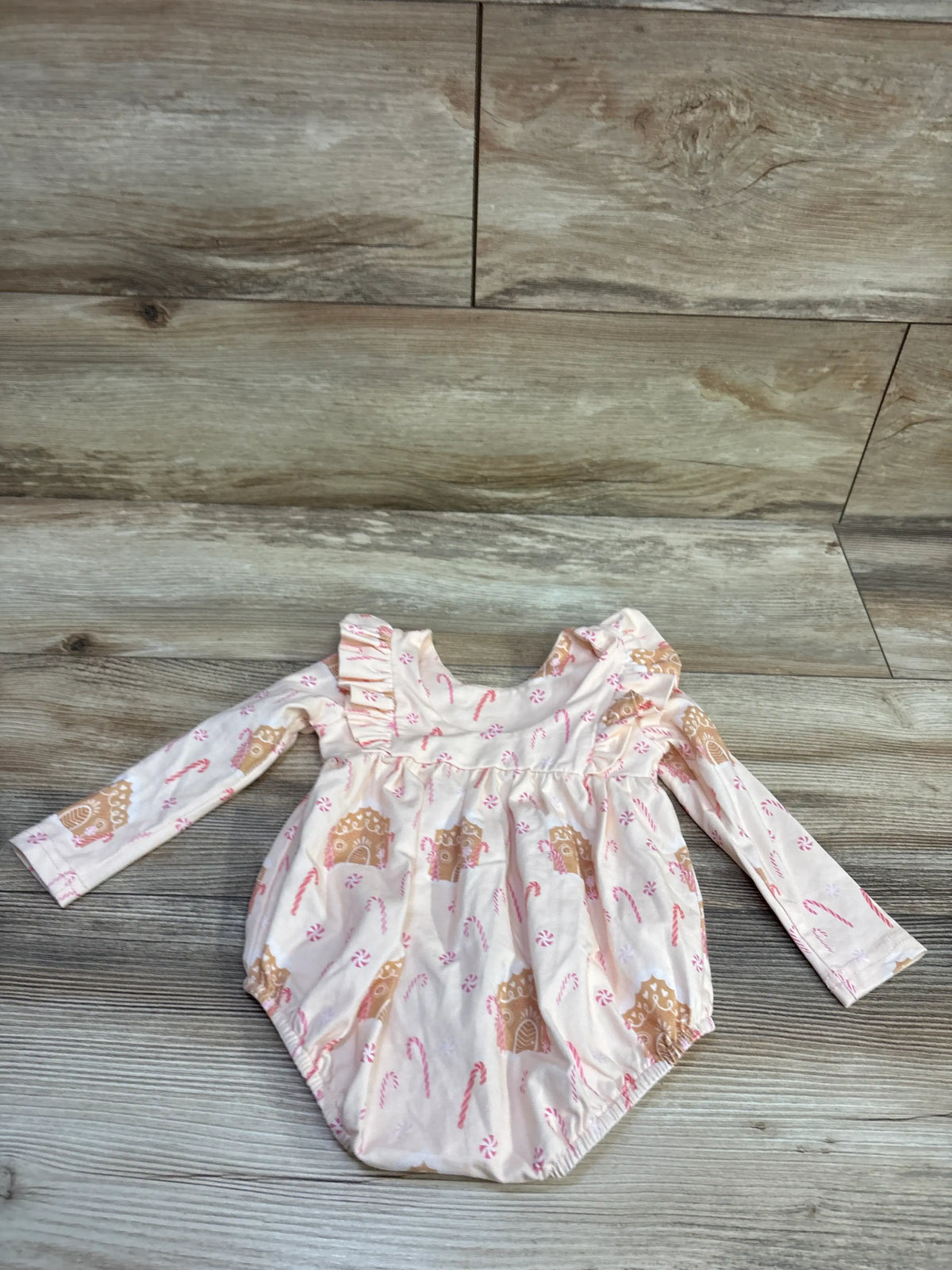 Front view of cream long sleeve bubble romper showcasing gingerbread house and candy cane print with wood floor background