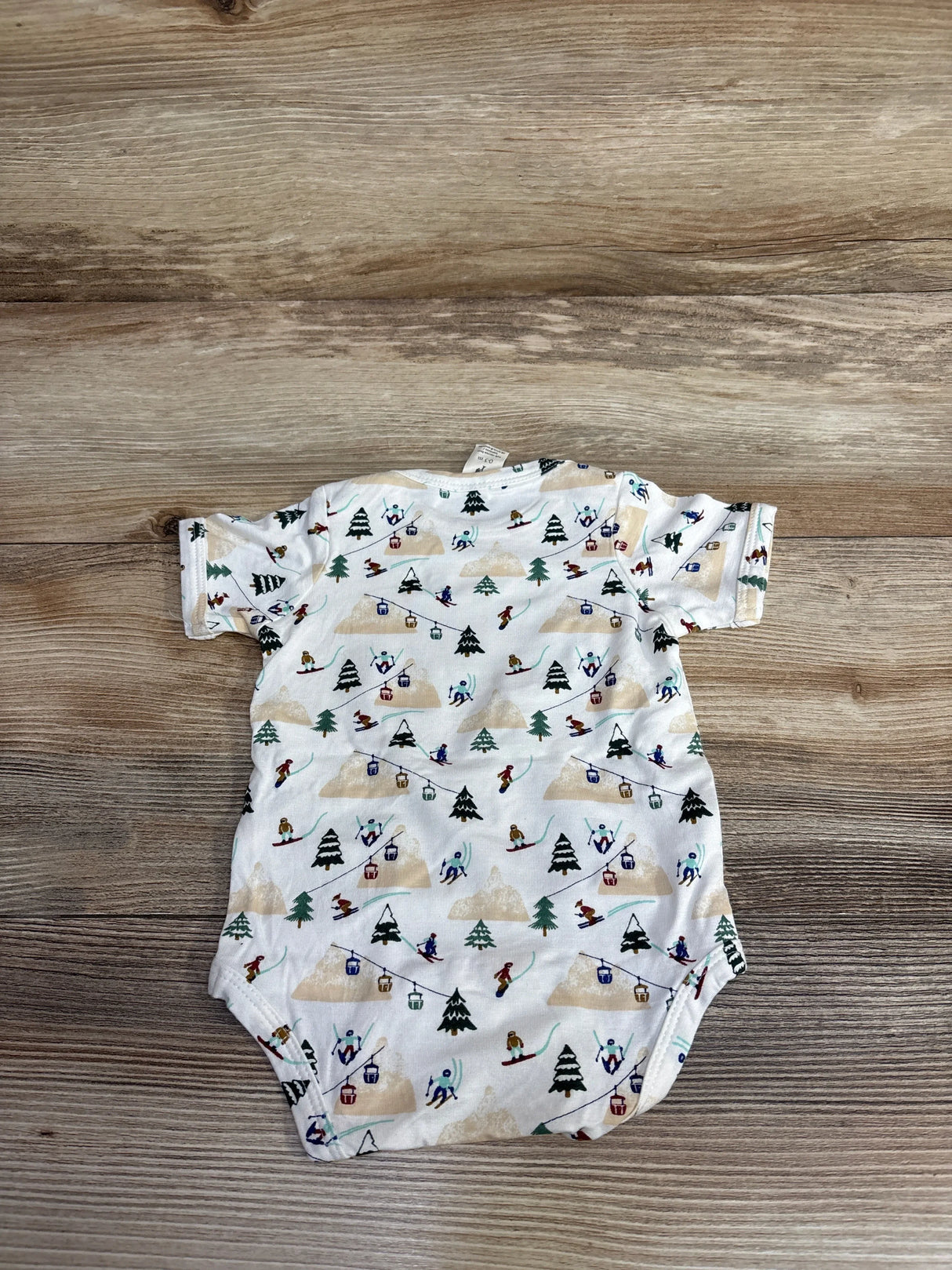 white baby onesie with colorful ski and snowboarding print on wooden floor