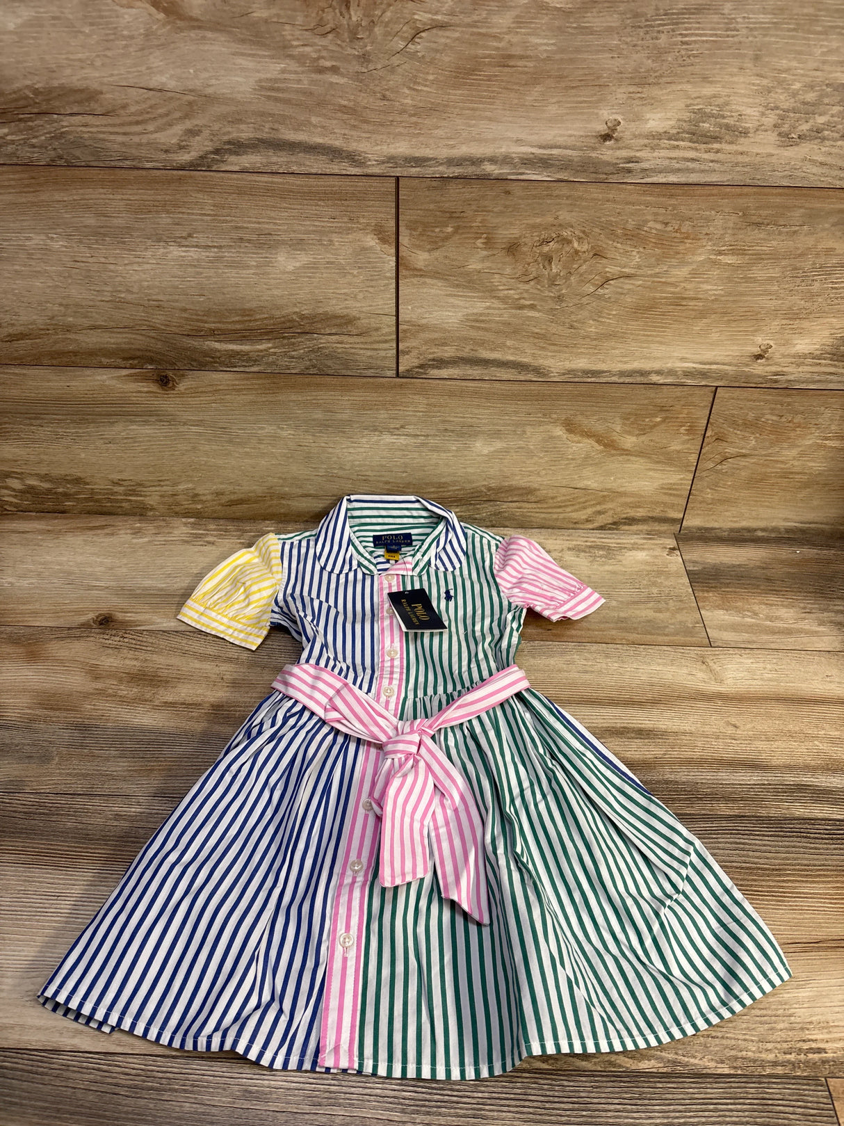 Flat lay of Polo Ralph Lauren shirtdress showing multicolor vertical stripes, tied pink waist sash on wood floor