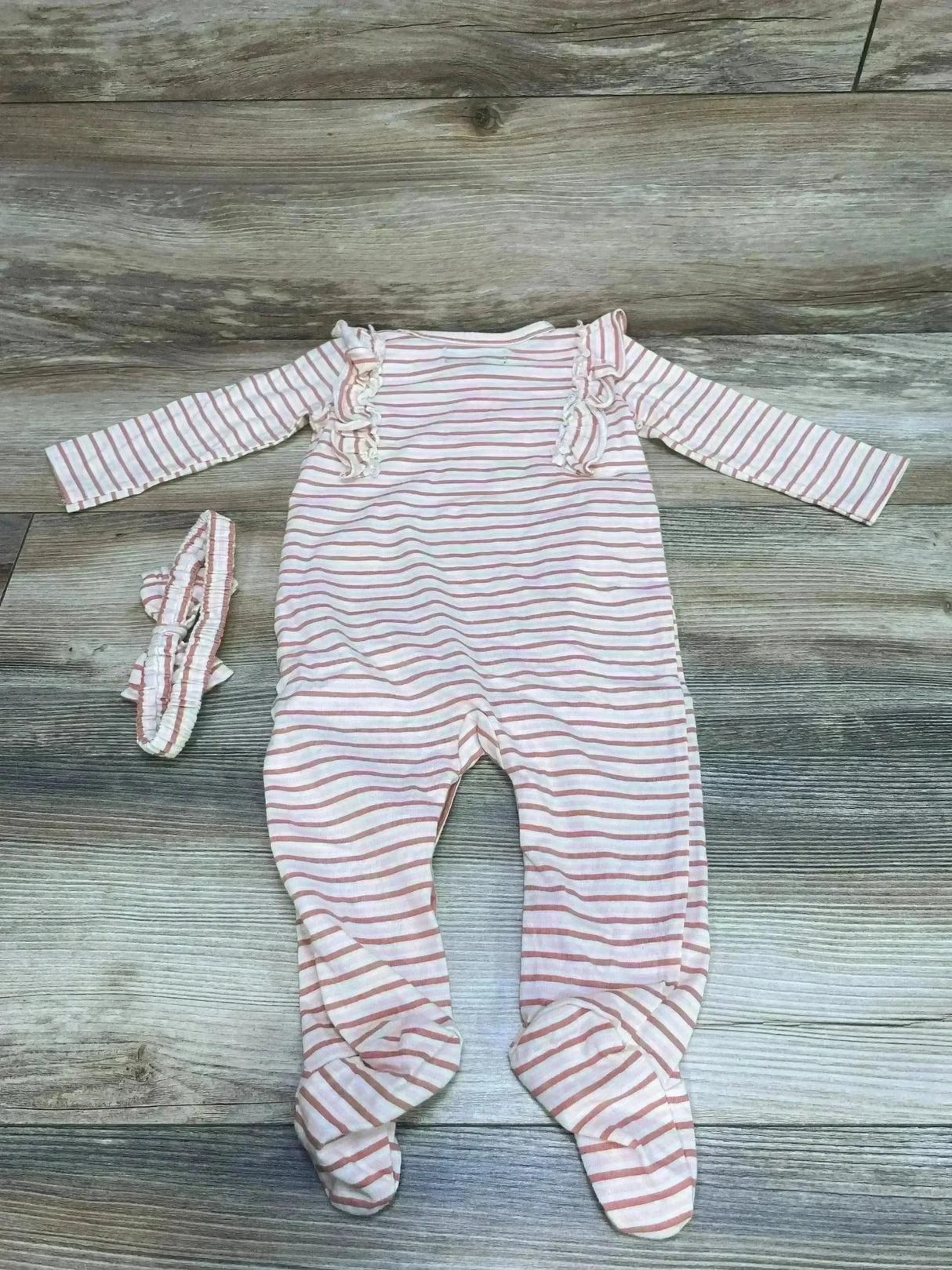 Top-down view of pink and white striped footed baby coverall with ruffle trim and matching headband on wood background, size 6-9 months