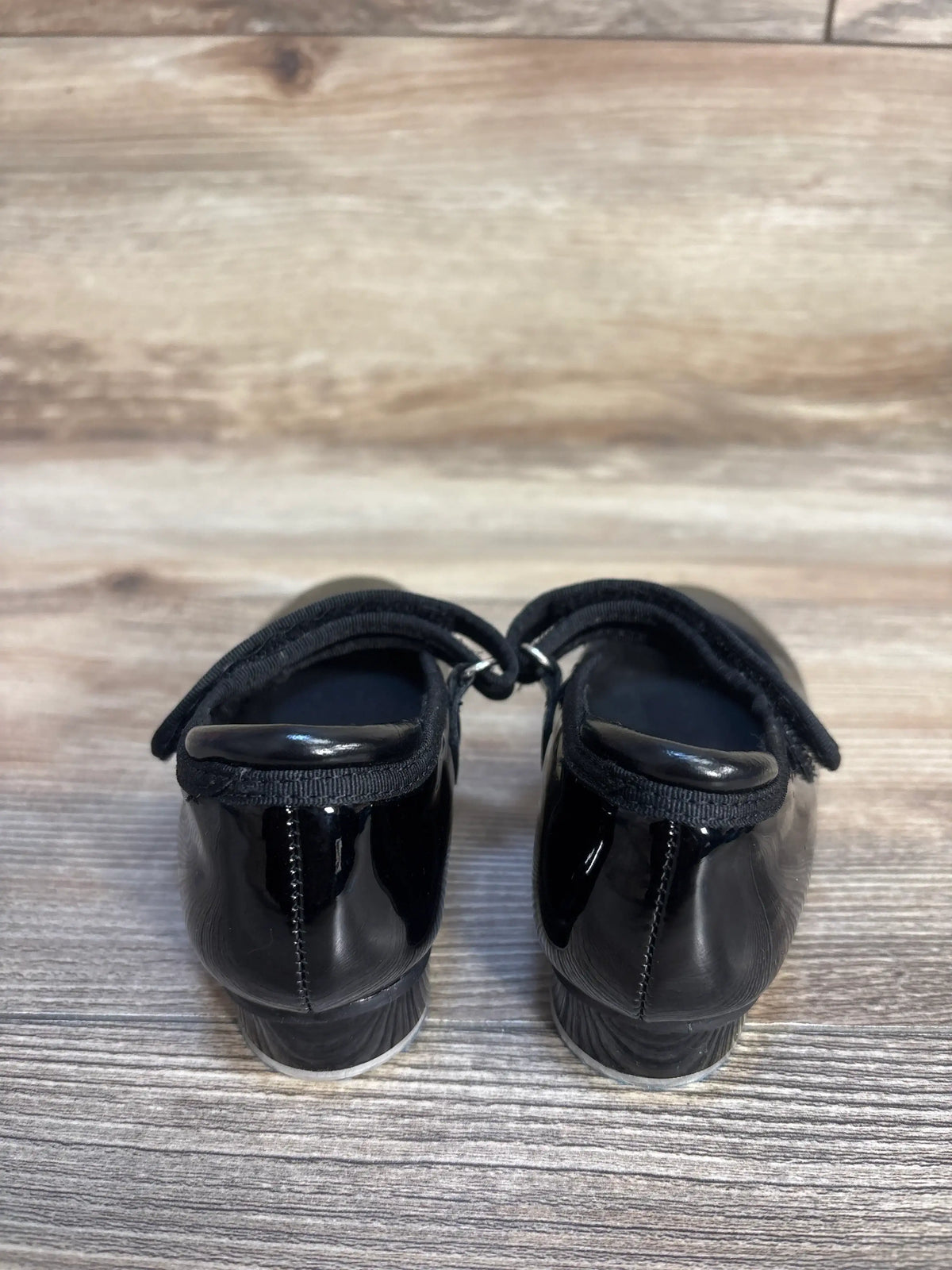Back view of Stelle girls black patent leather tap shoes size 7C showcasing low heel and strap closure on wood floor