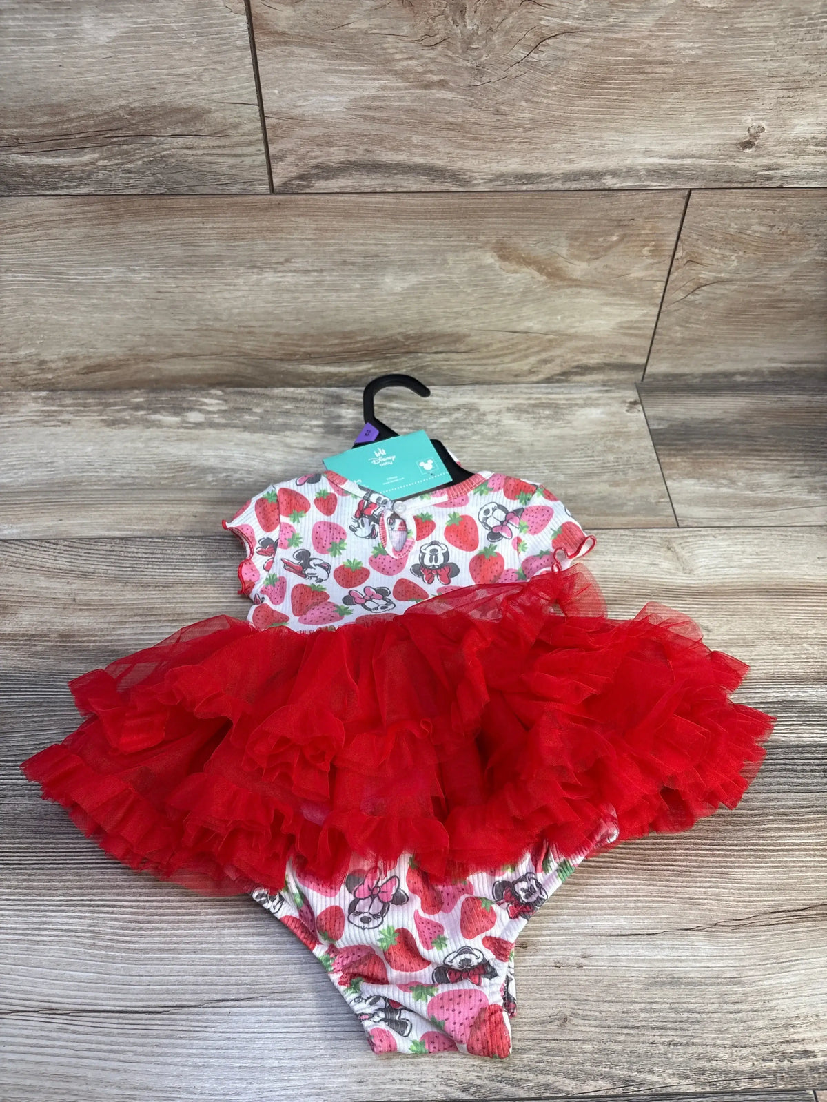 Flat lay of Disney Baby Minnie Mouse bodysuit and headband showcasing red layered tulle tutu and strawberry print on wood background