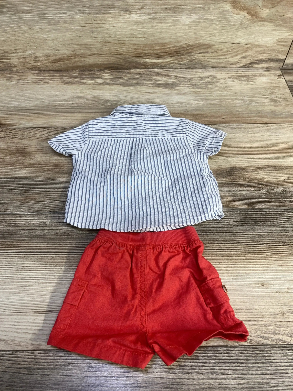 Flat lay of newborn Just One You 2-piece: white striped button-up shirt and red elastic-waist shorts with pockets on wood background
