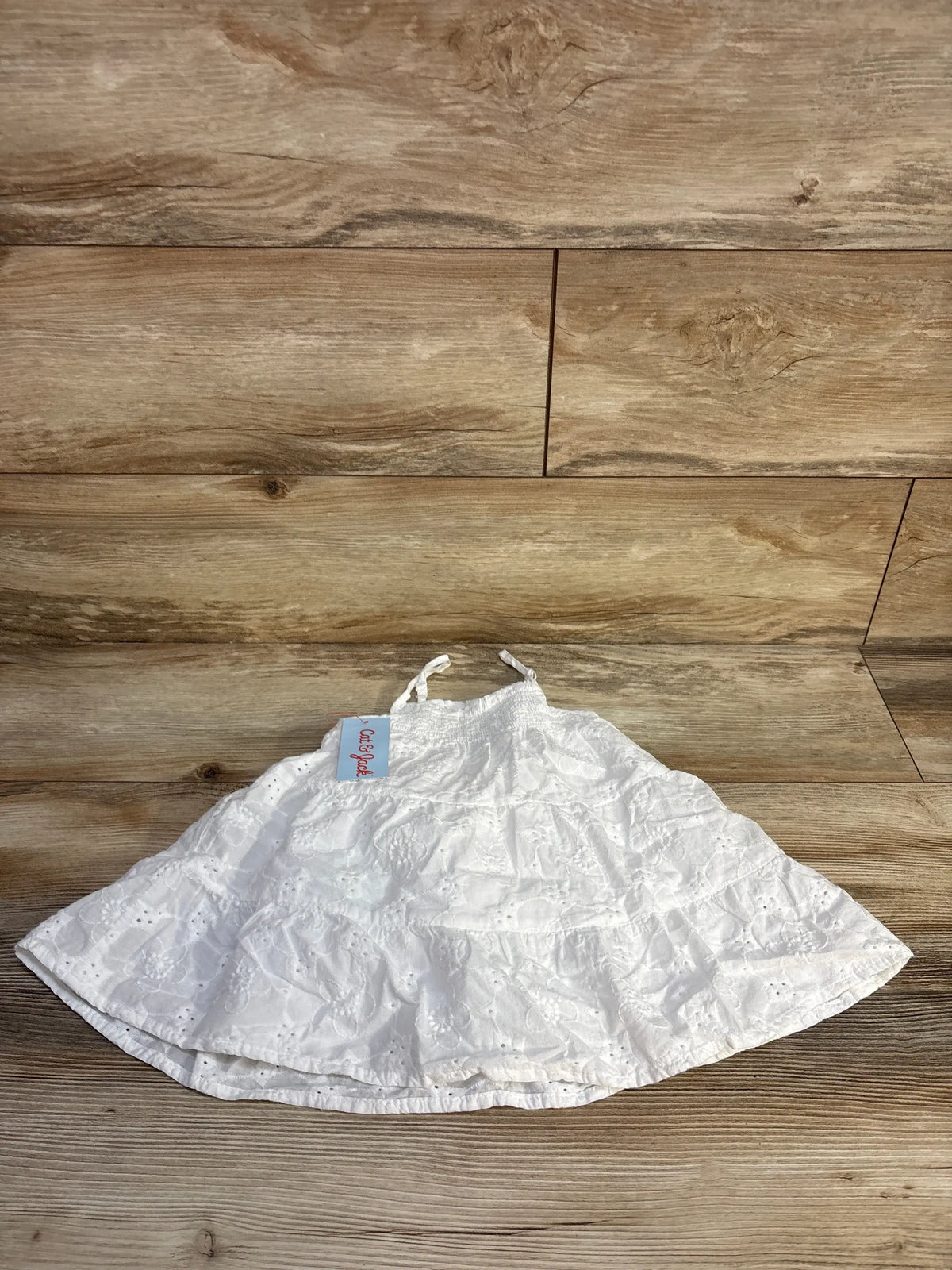 Front view of a white Cat and Jack eyelet embroidered dress showcasing sleeveless tiers and a smocked upper on a wood floor