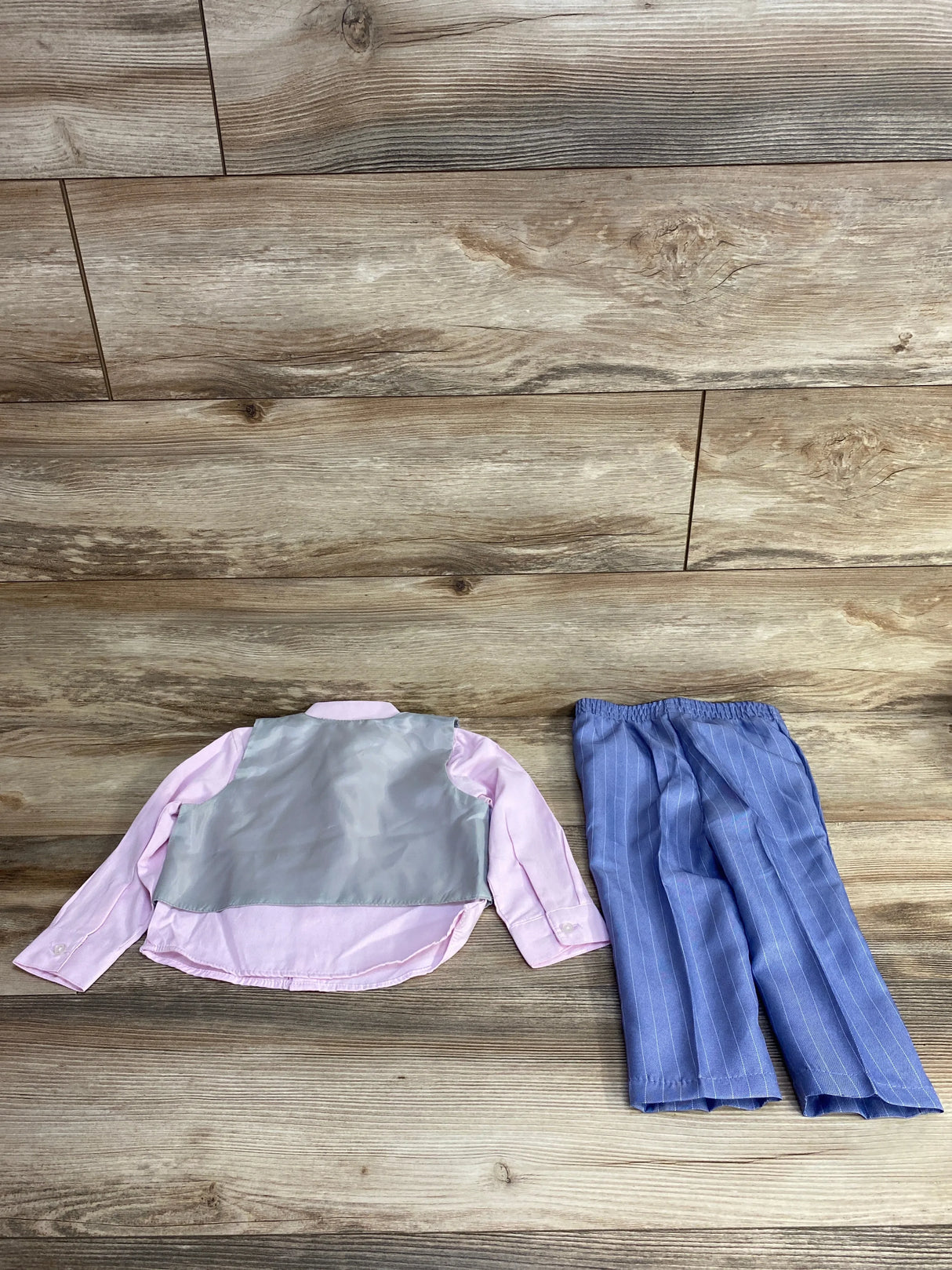 Back view of toddler pink long sleeve shirt with silver vest back and blue pinstripe elastic waist pants on wood floor