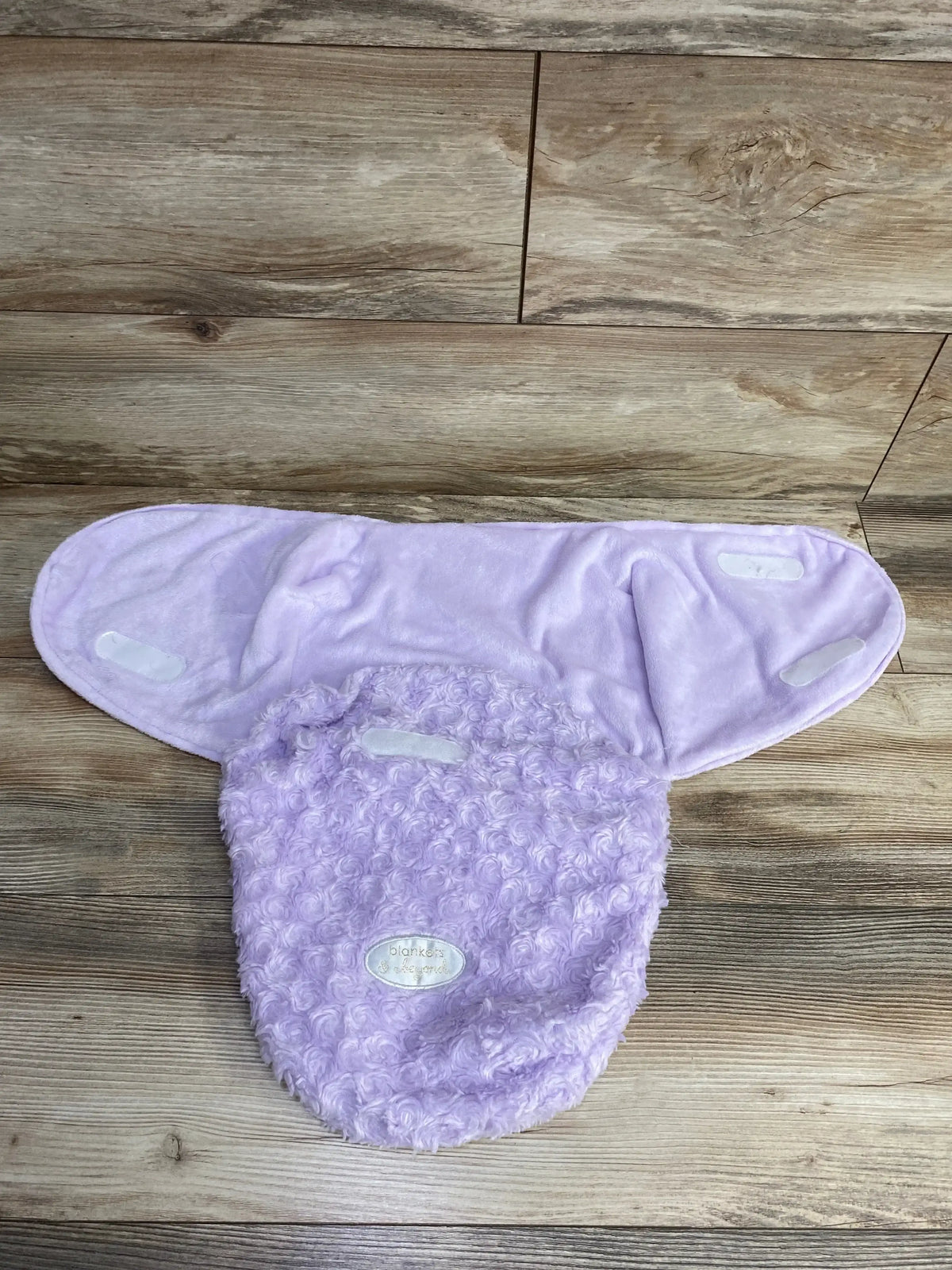 Lilac plush baby swaddle blanket with soft textured fabric and Velcro straps on wood floor