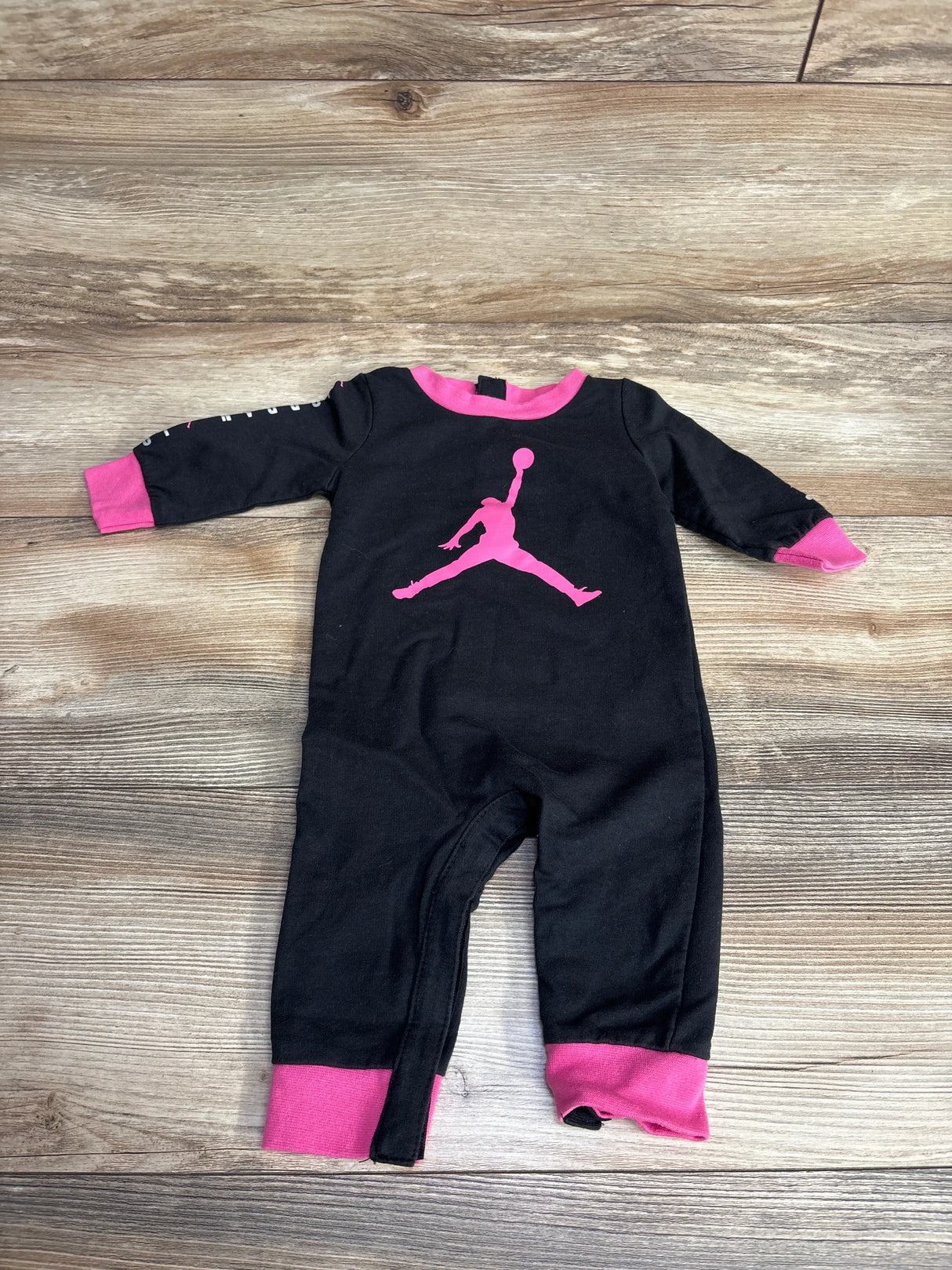 Black and pink infant jumpsuit featuring a pink basketball player silhouette on front, laid on wooden floor
