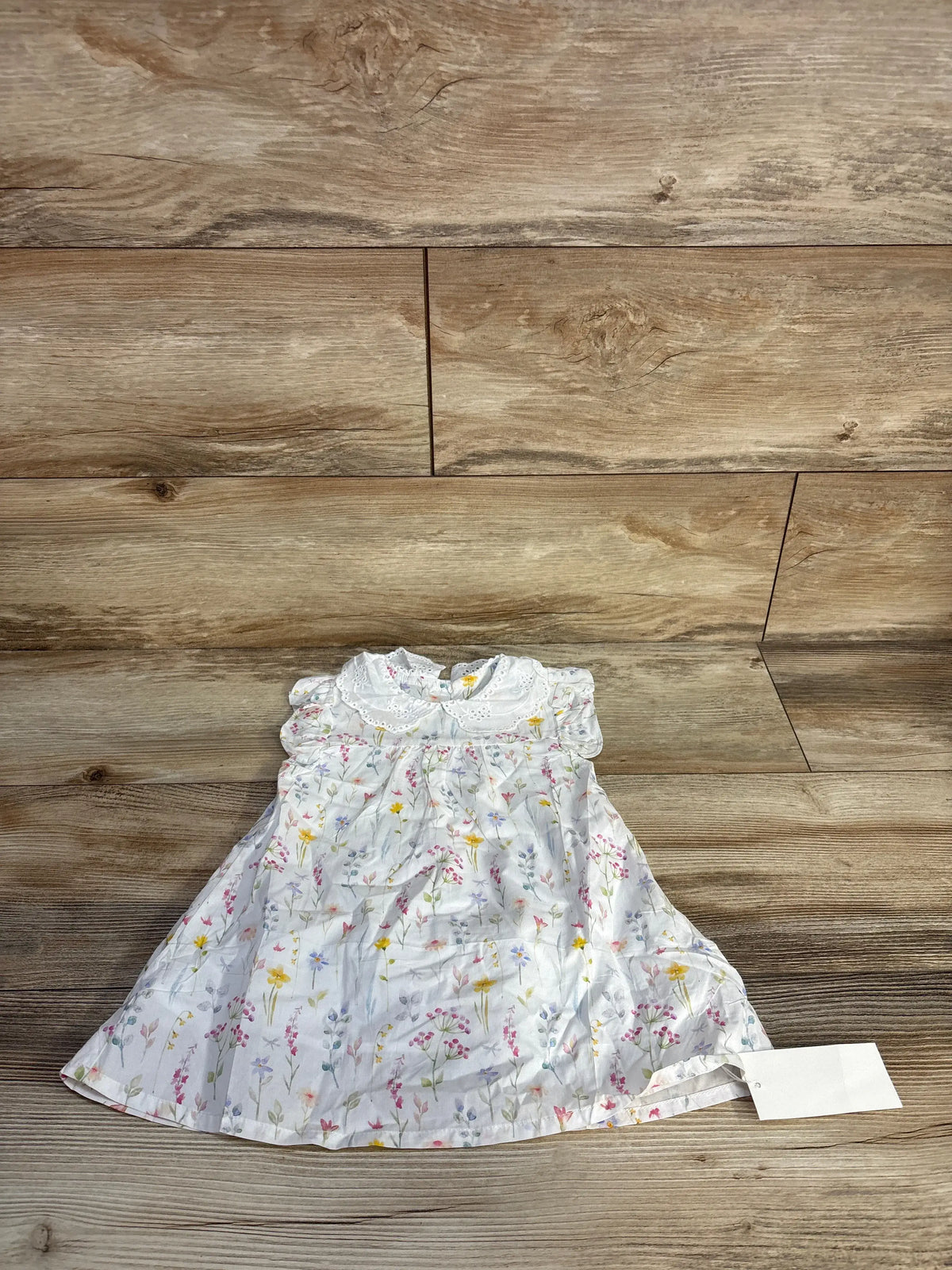 Front view of SimpleKids white floral eyelet collar dress showcasing the eyelet collar on a wood floor