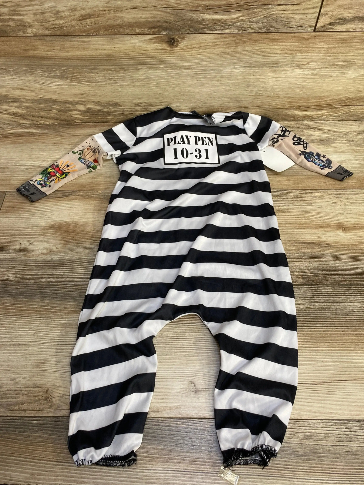 Flat lay of convict costume with black and white stripes, PLAY PEN 10-31 chest patch and printed sleeves on wood floor