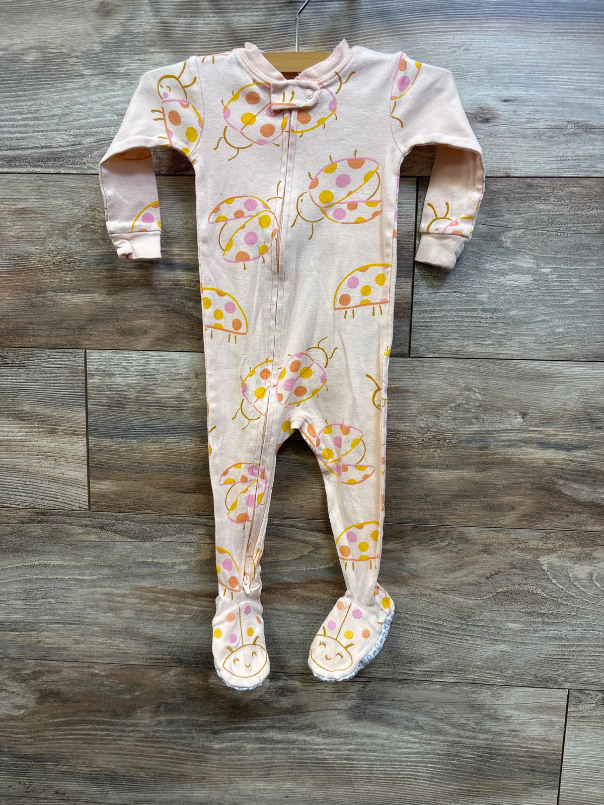 Front view of Carter’s peach footed sleeper showcasing ladybug print and front zipper on a wood floor