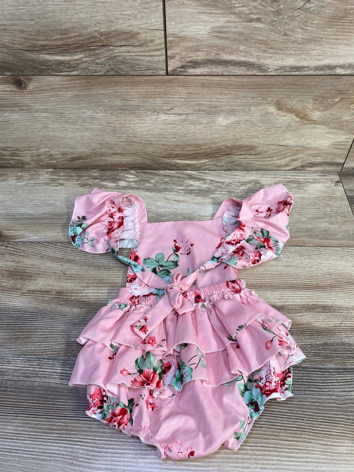 Flat lay of pink floral ruffle bubble romper size 6-9M showing tiered ruffle skirt, bow at back and puff sleeves on wood background