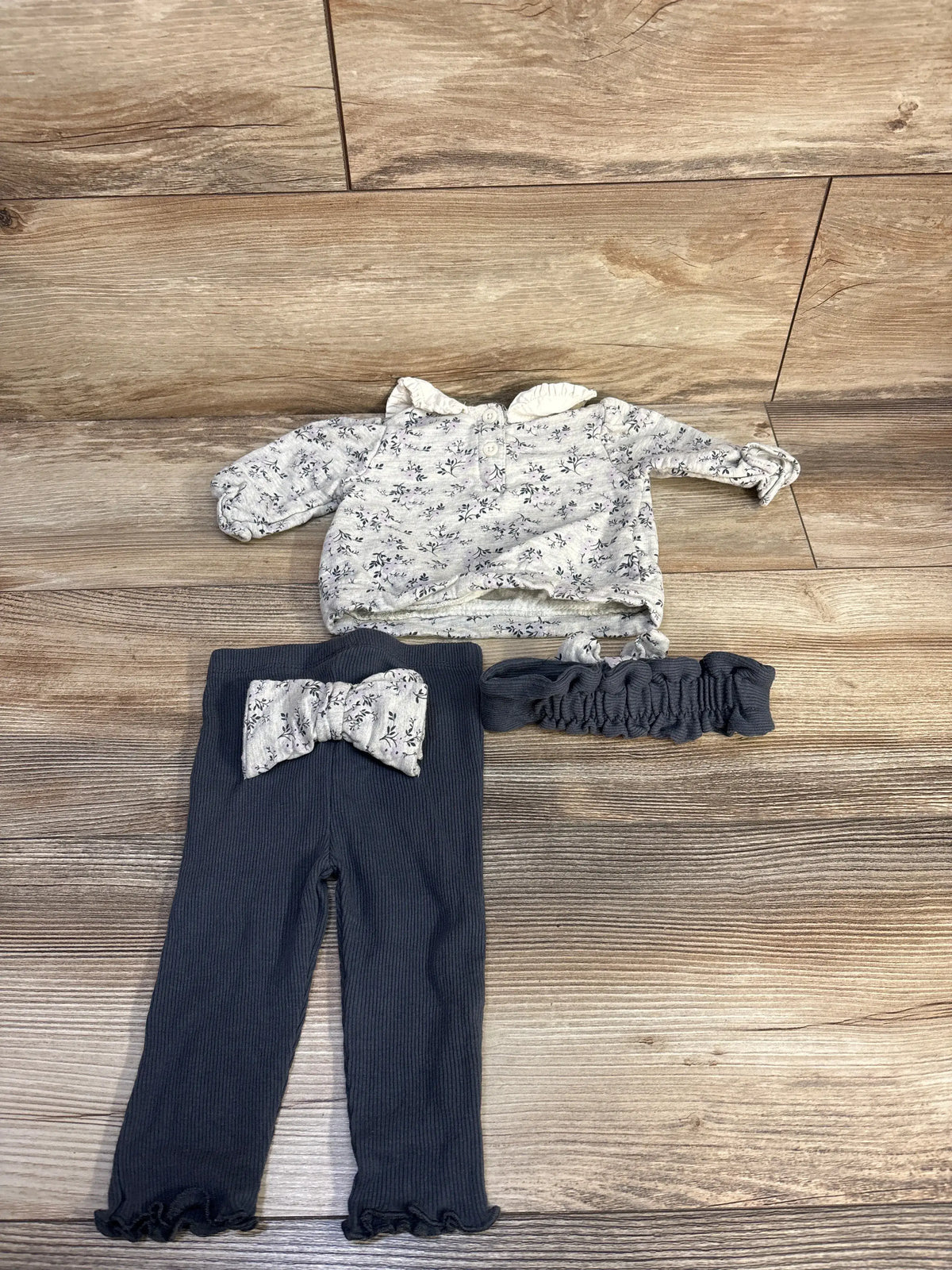 Top-down view of Nicole Miller three-piece grey baby set with floral sweatshirt, ribbed leggings, and headband