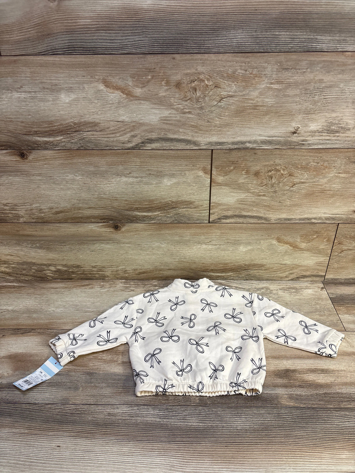 Back view of Cat & Jack quarter-zip sweatshirt with ivory fabric, black bow print and elastic hem on light wood background