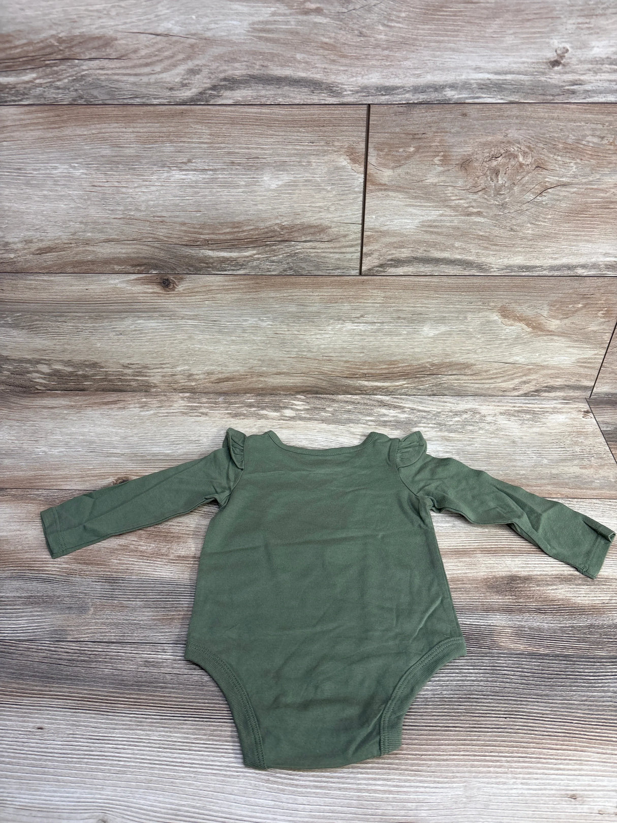 Olive green long-sleeve baby onesie with ruffle shoulder details on wood floor