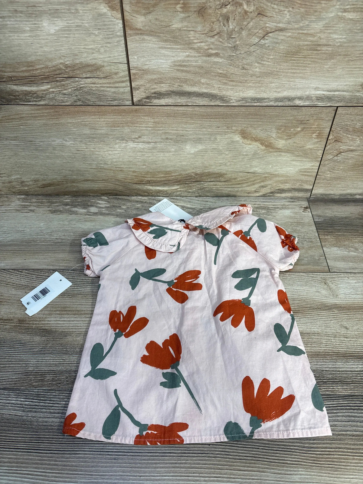 Front view of pink 7 For All Mankind floral button-up shirt in size 24 months, with orange and green flowers on a wood floor