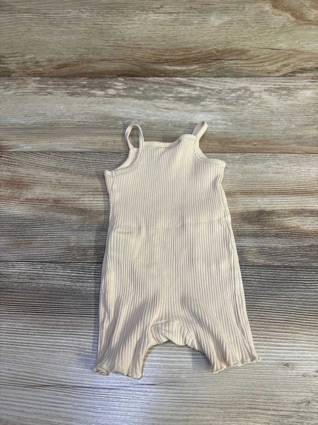 Flat lay of beige ribbed tank shortie romper showing thin shoulder straps and ribbed texture on light wood background