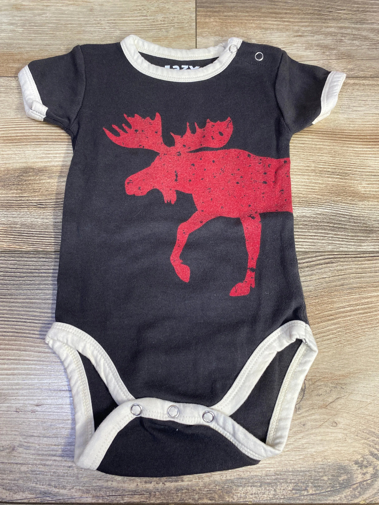Black baby onesie with red moose graphic and white trim on wood background