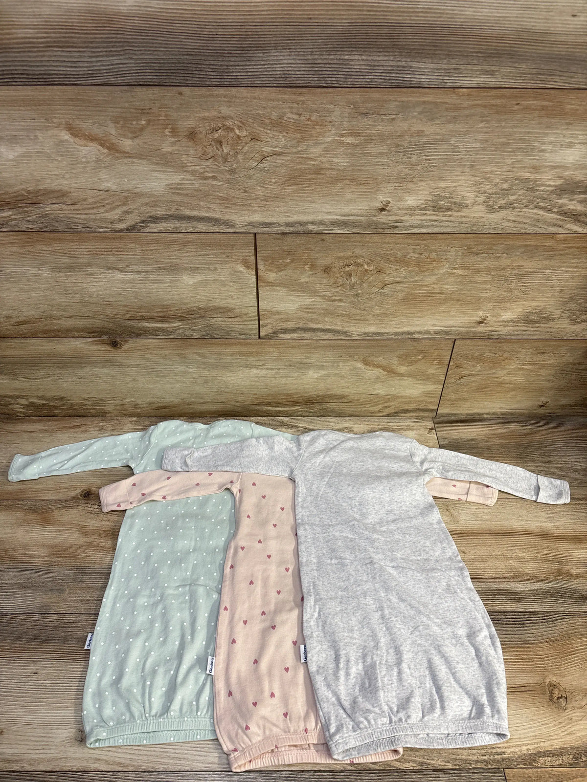 Overhead view of Gerber three-pack baby sleep gowns showcasing mint, pink, and gray gowns on a wood floor