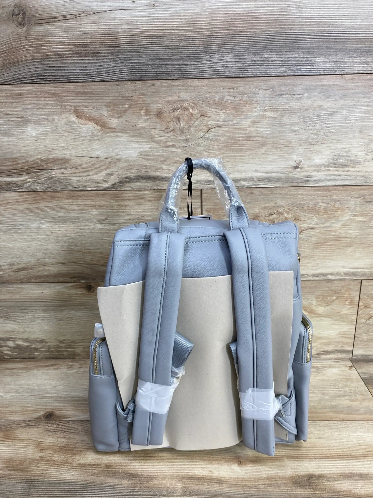 Light gray backpack diaper bag with adjustable straps, side pockets, on wood background
