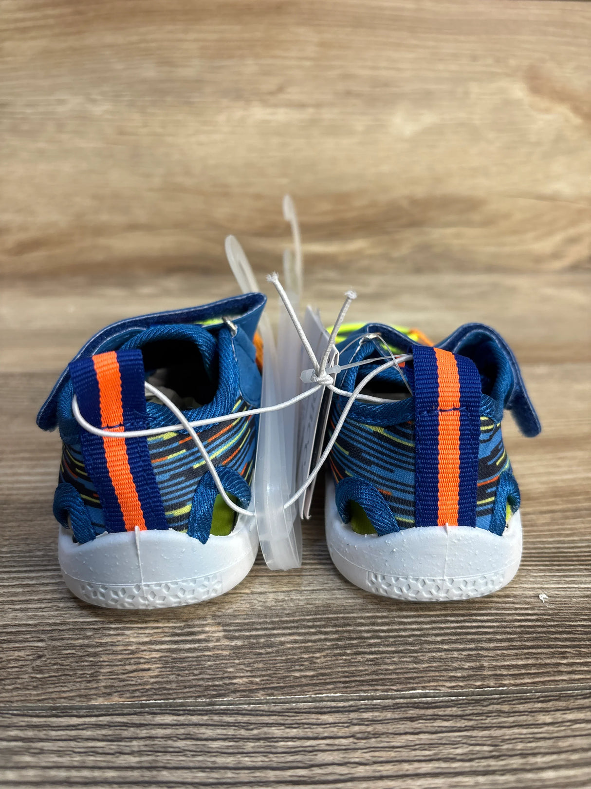 Rear view of blue and orange striped toddler shoes with tags attached, on wood surface