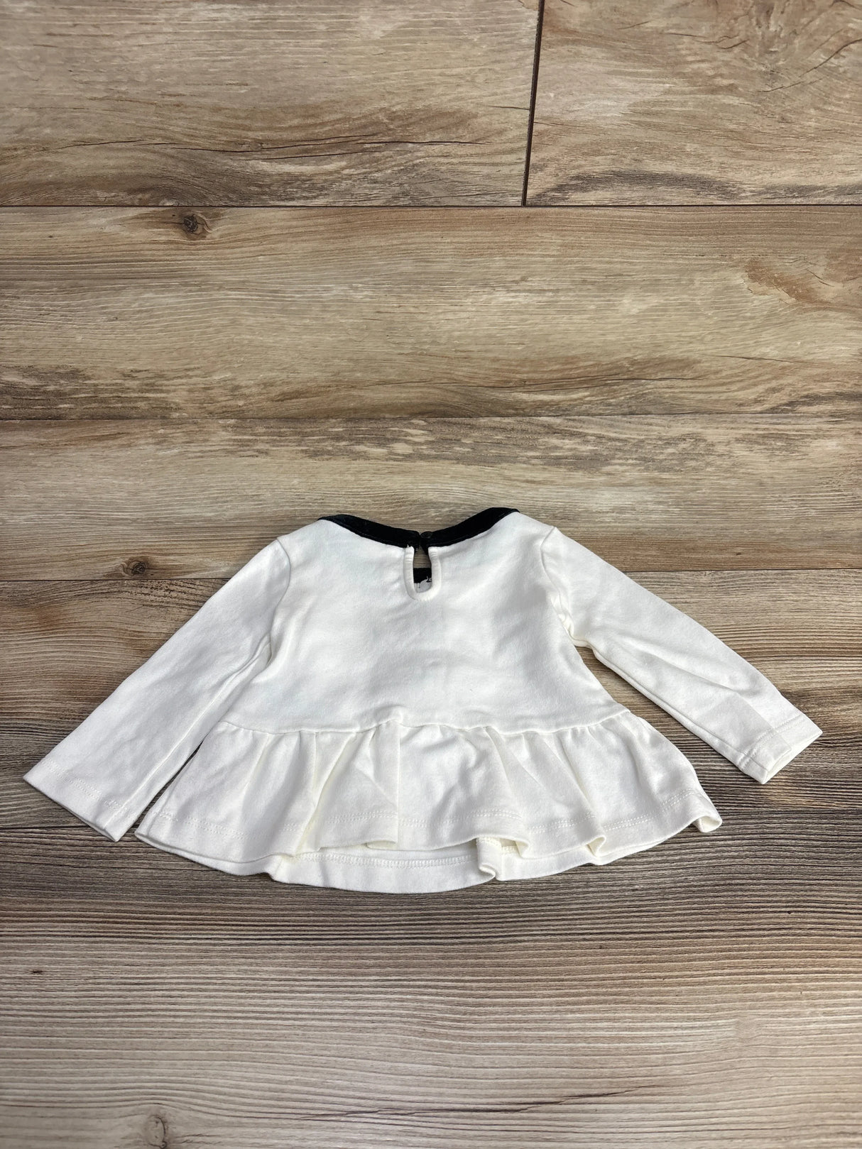 White long sleeve baby shirt with ruffle hem and back button on wood background