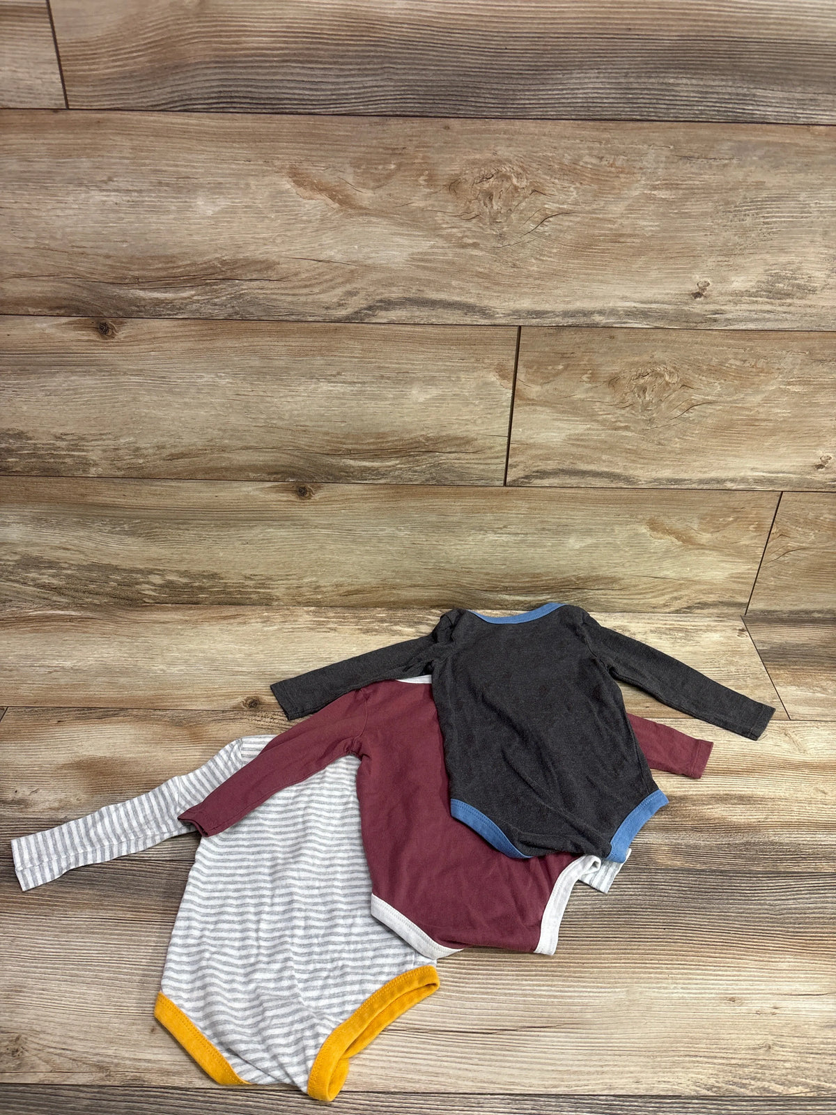 Top-down view of Harry Potter three pack long sleeve bodysuits in black, burgundy, and gray stripes on a wood surface