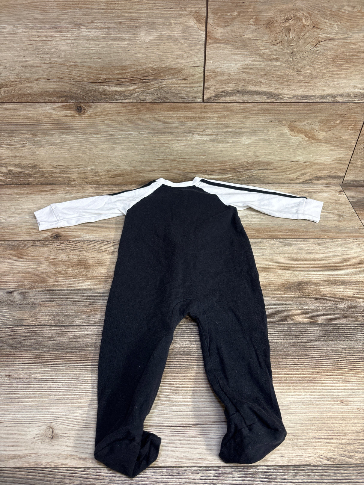 Black and white long-sleeve baby onesie with footies laid flat on wood background
