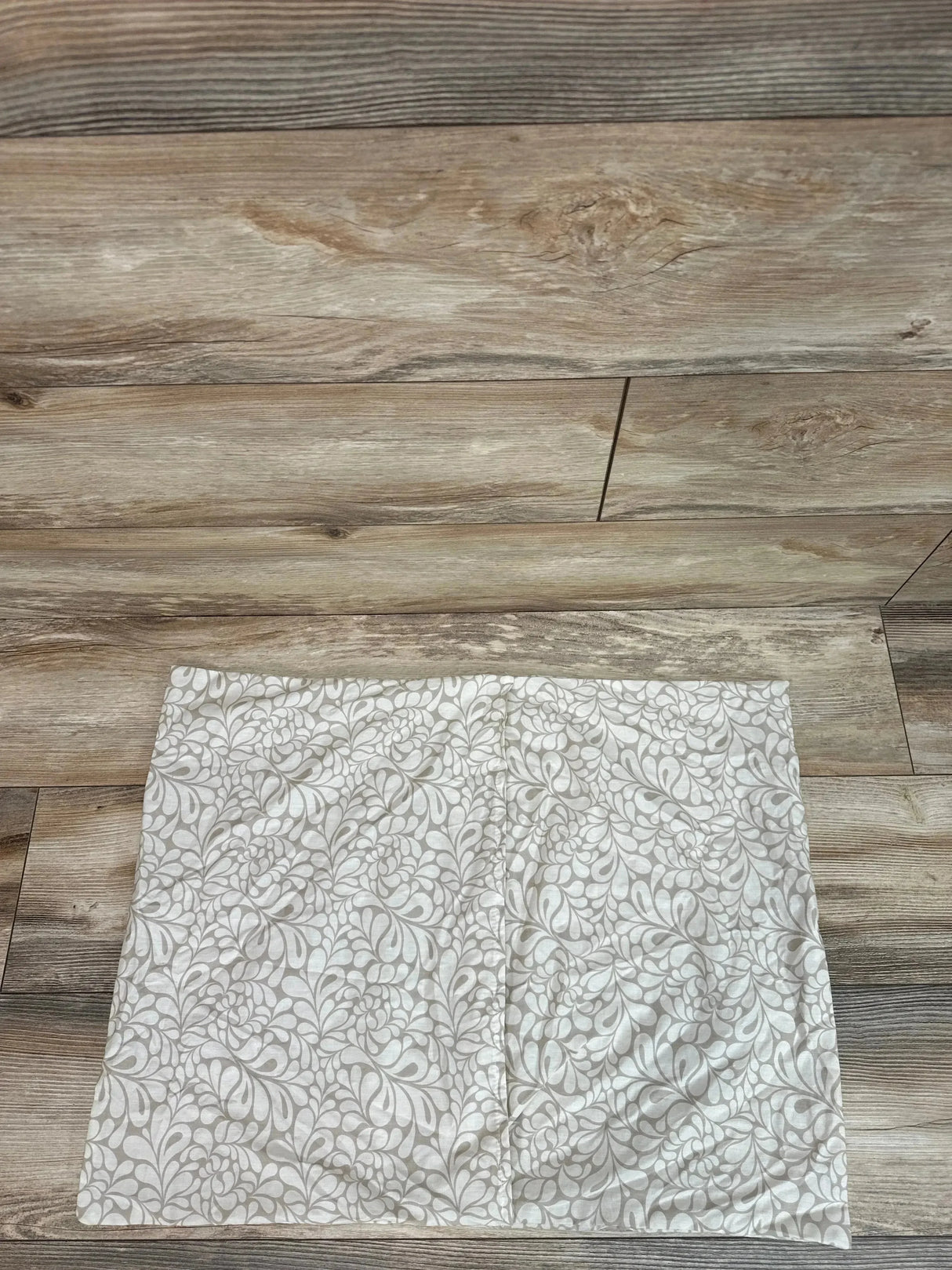 Top-down view of Leachco Back 'N Belly On My Own pillow cover in Chic Splash Taupe showing taupe floral swirl on wood floor