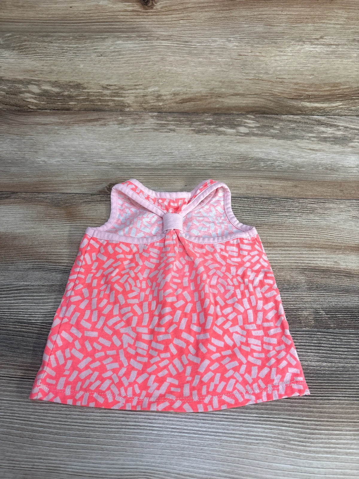Flat-lay of Okie Dokie tank top 9m showing pink fabric with white sprinkle print and back bow on wood background
