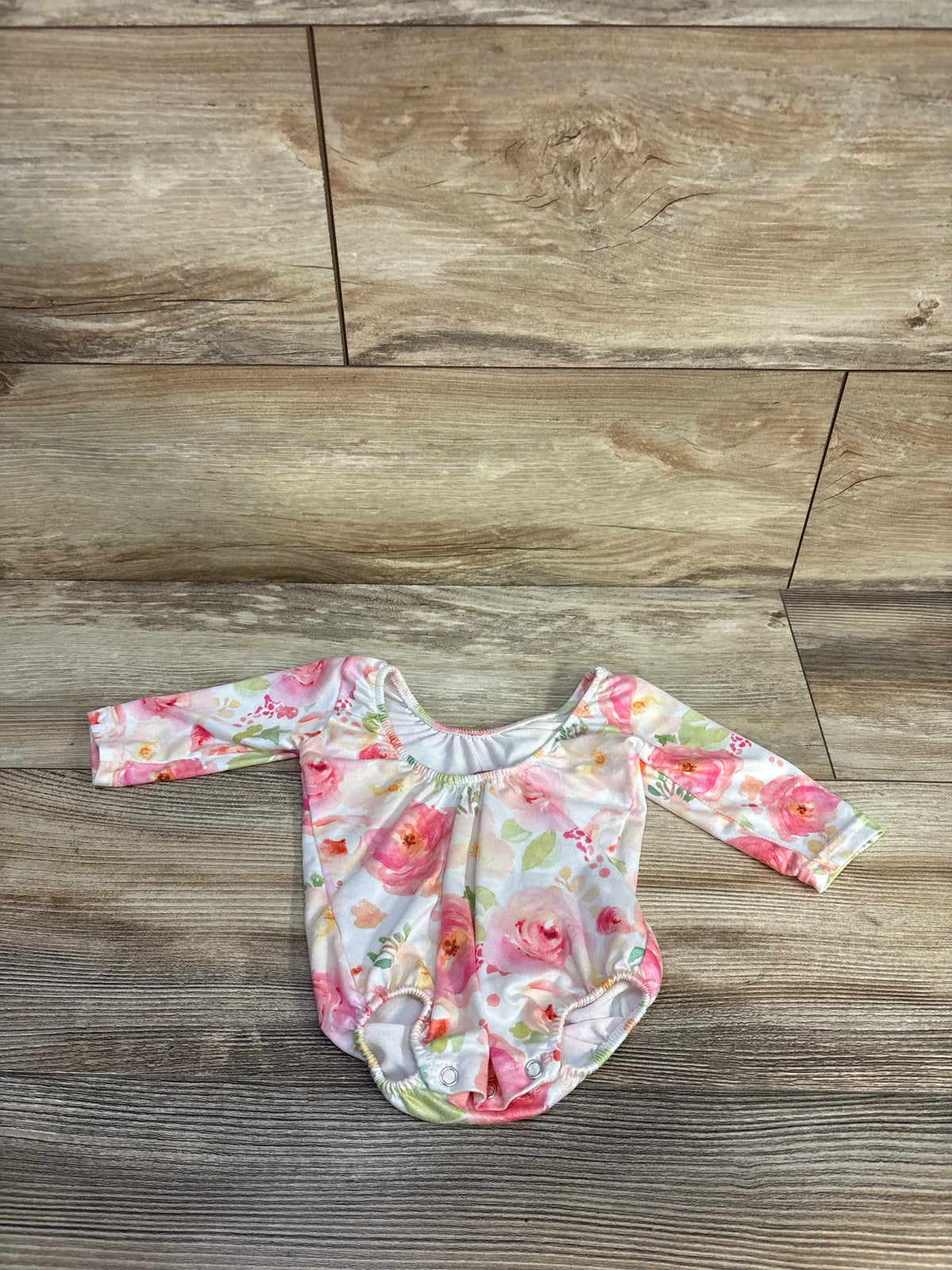 Front view of Castle Rose Boutique floral leotard in white showcasing long sleeves and snap closures with a wood-grain background