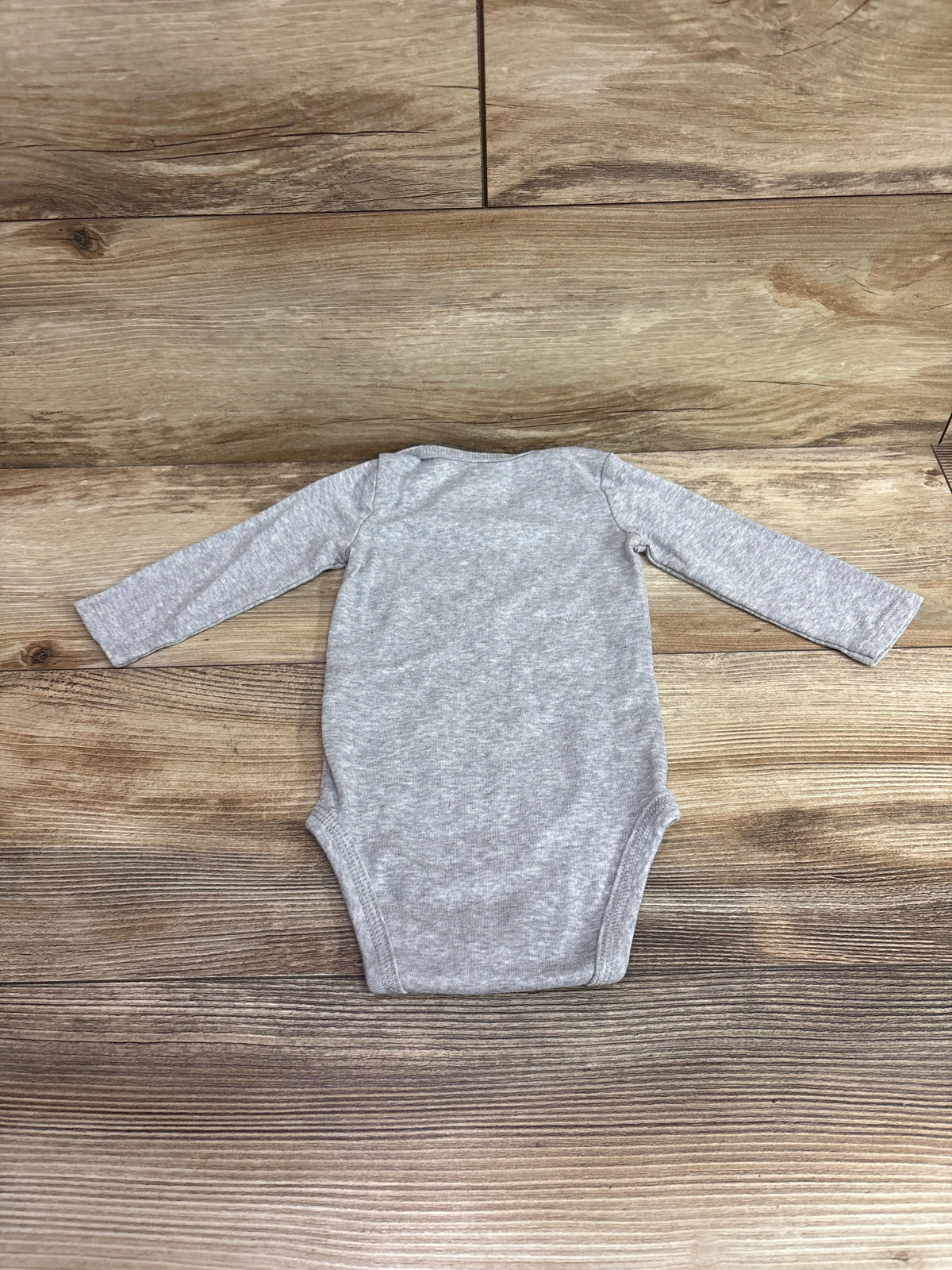 Top view of grey Just One You Little Boo bodysuit, size 6 months, with long sleeves on a wood-look floor