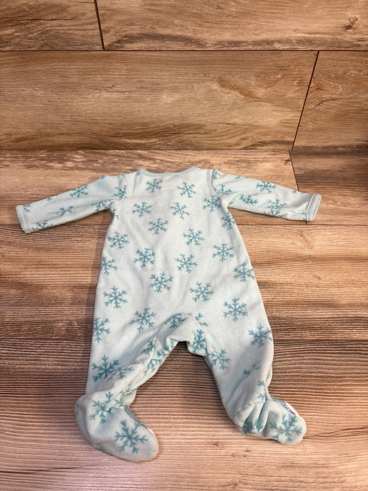 Front view of a blue snowflake blanket sleeper with long sleeves and attached footies on a wood floor